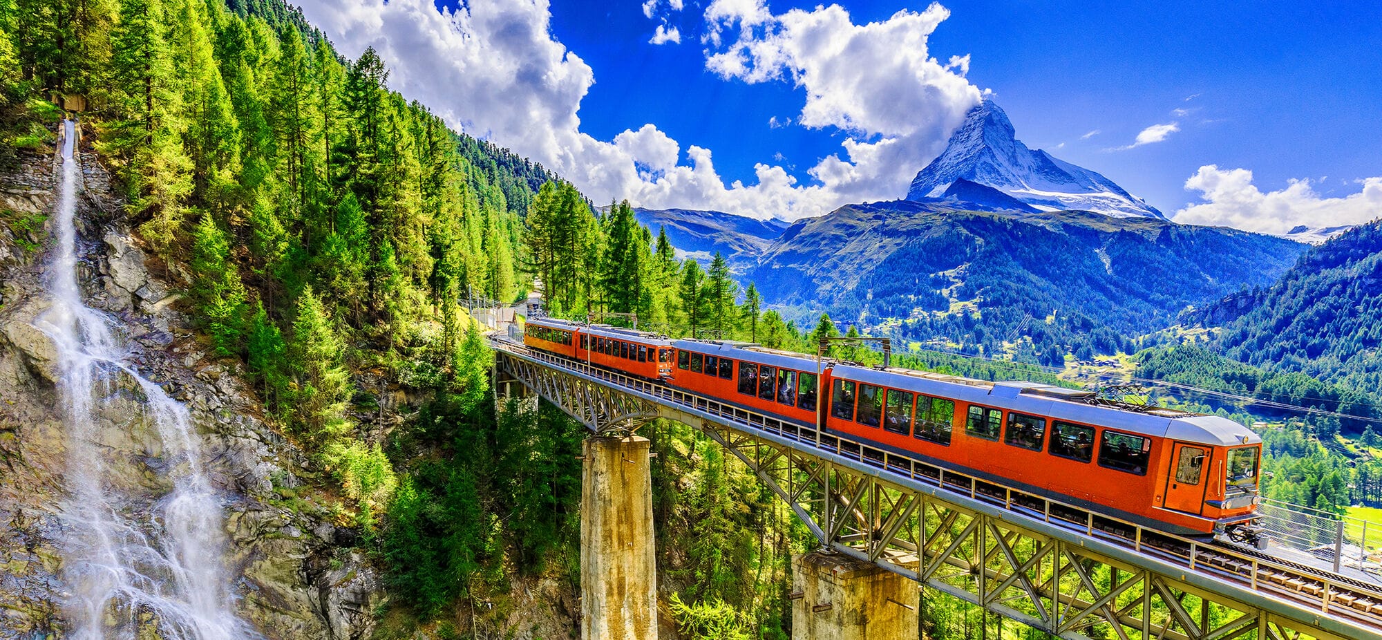 A red train travelling over a viduct with the Matterhorn mountain in the distance. 