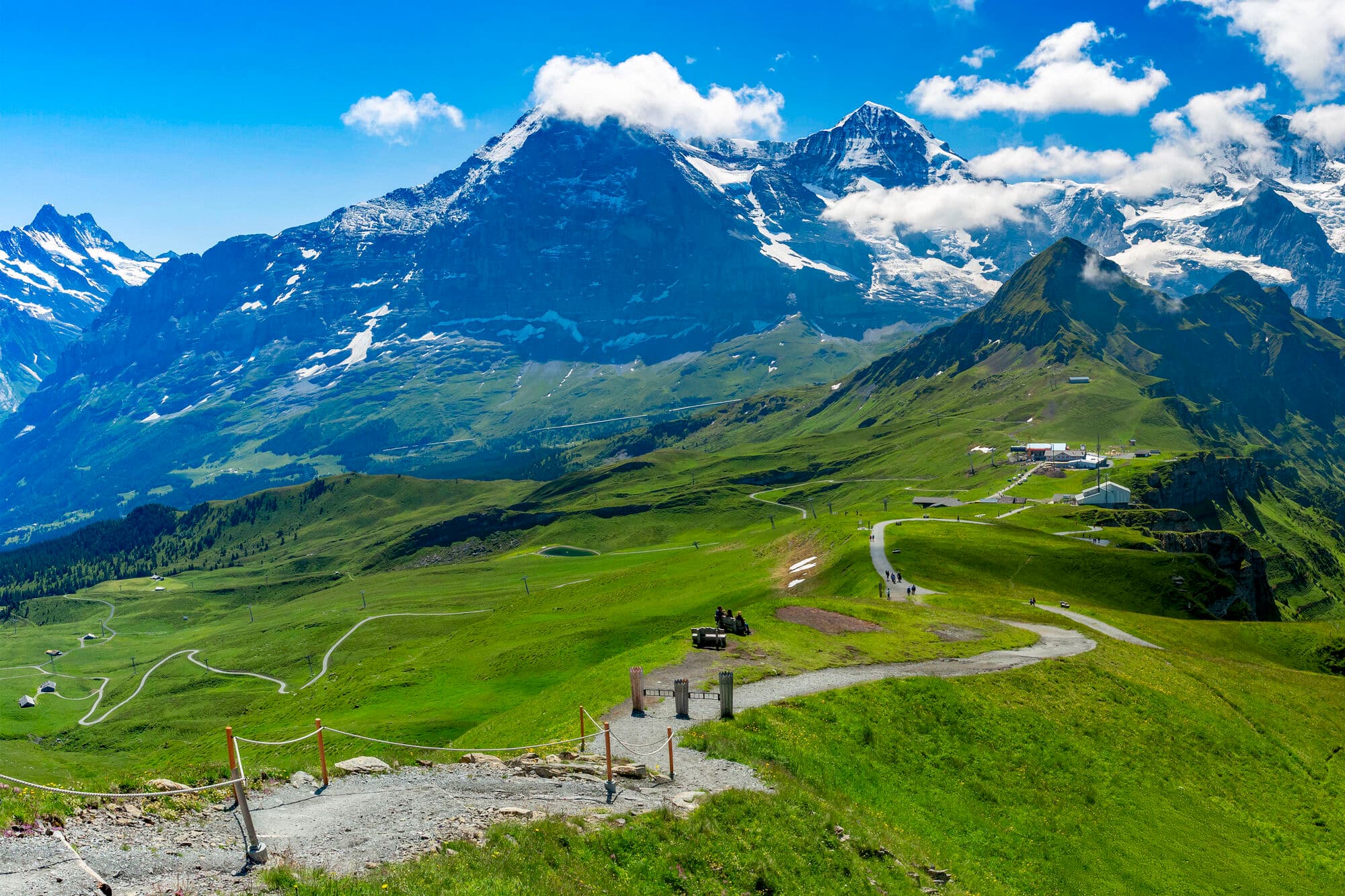 A pathway winding across a grassy meadow towards a mountain peak.