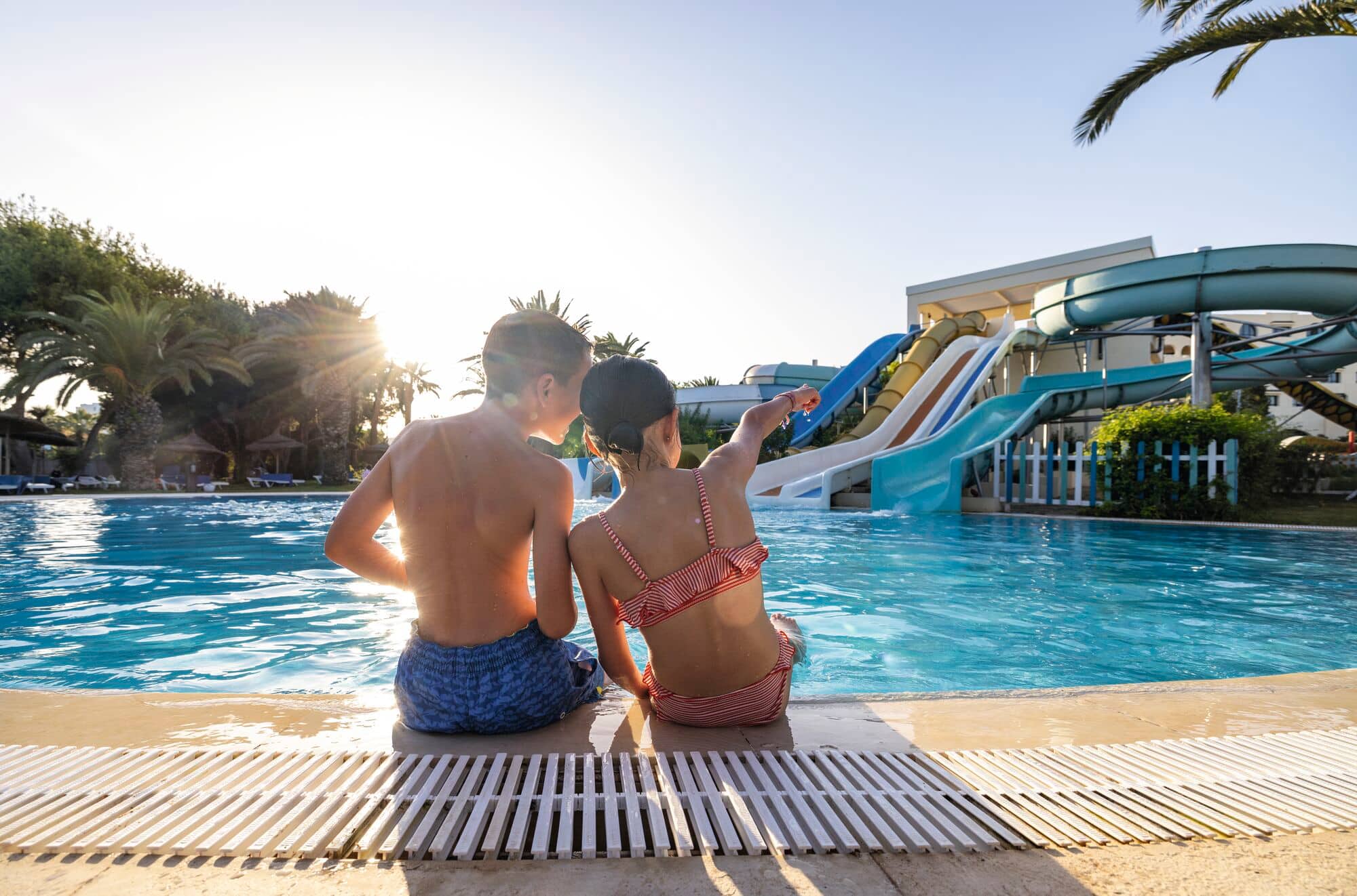  Children sitting by a pool, with waterslides in the background.