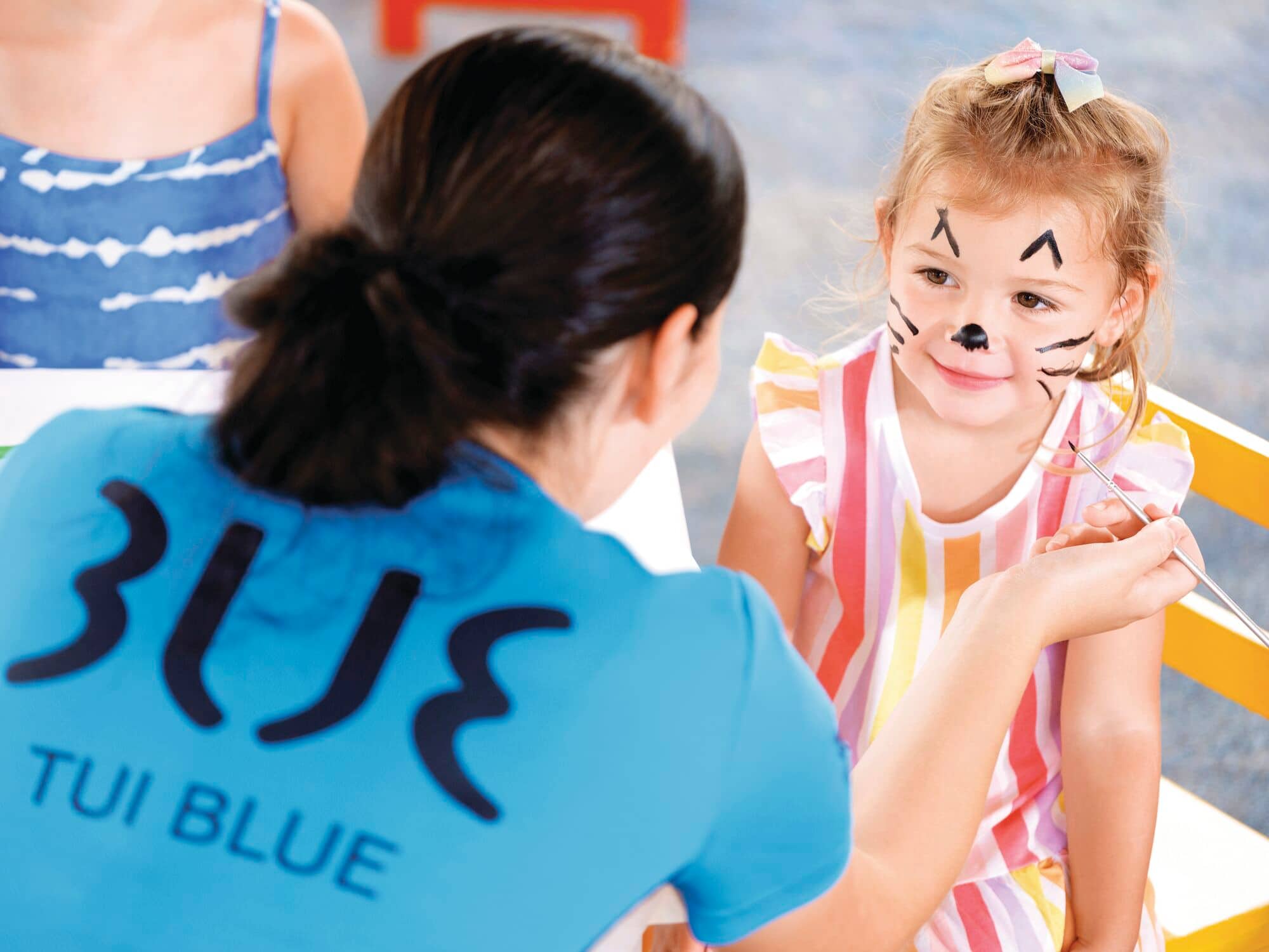 Kids club worker putting facepainting little girls face.
