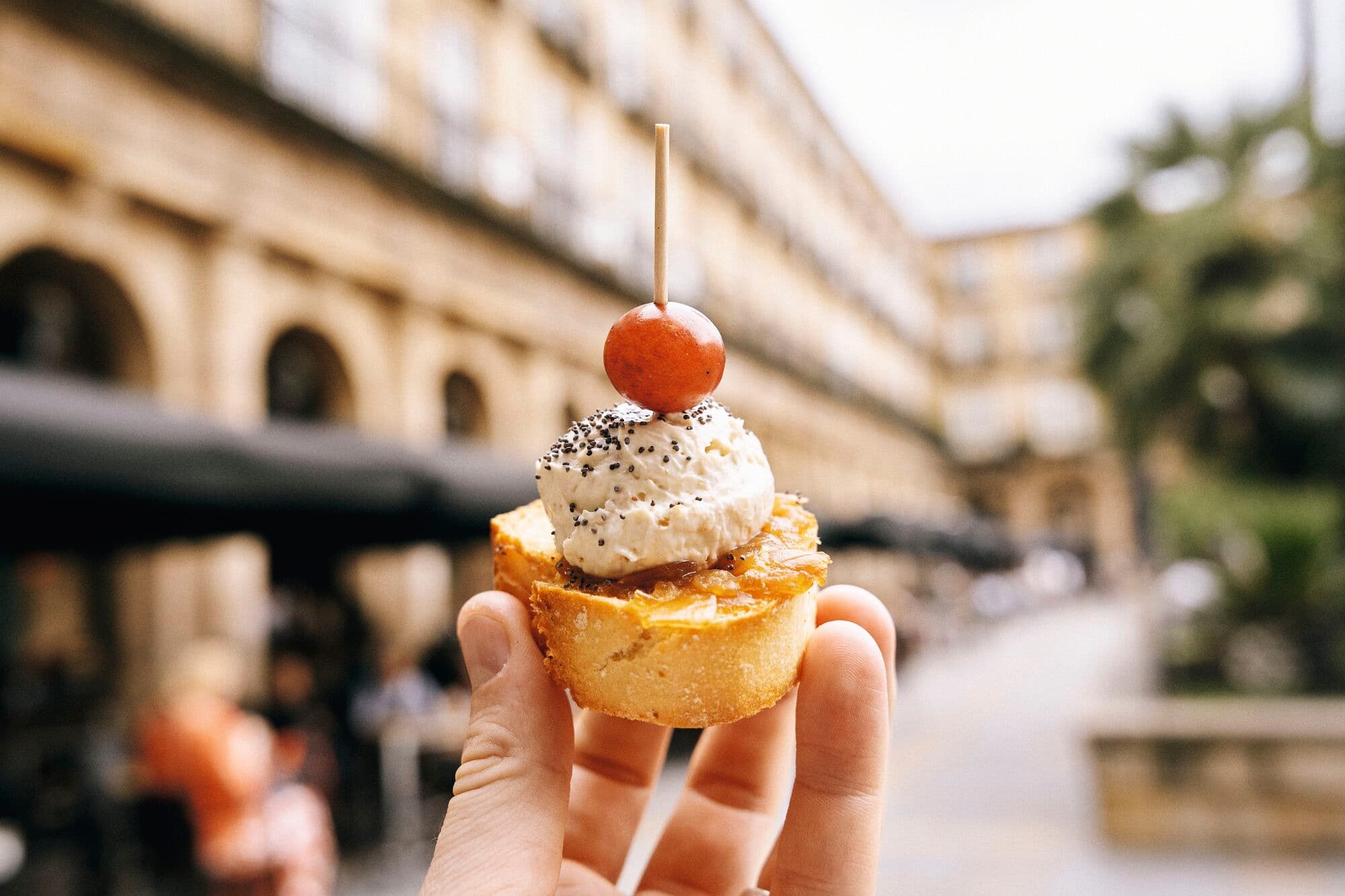 A close-up of a hand holding a pastry in front of an old town.