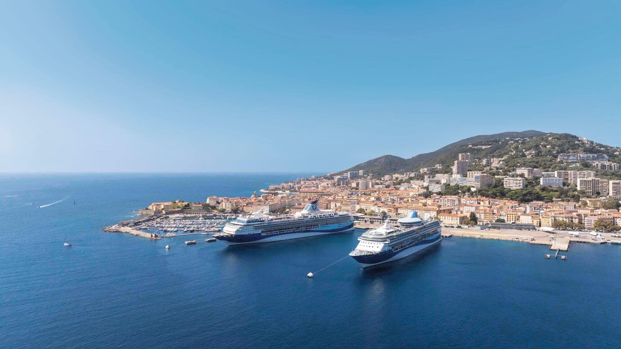 An aerial view of two Marella cruise ships anchored in a sunny harbour.