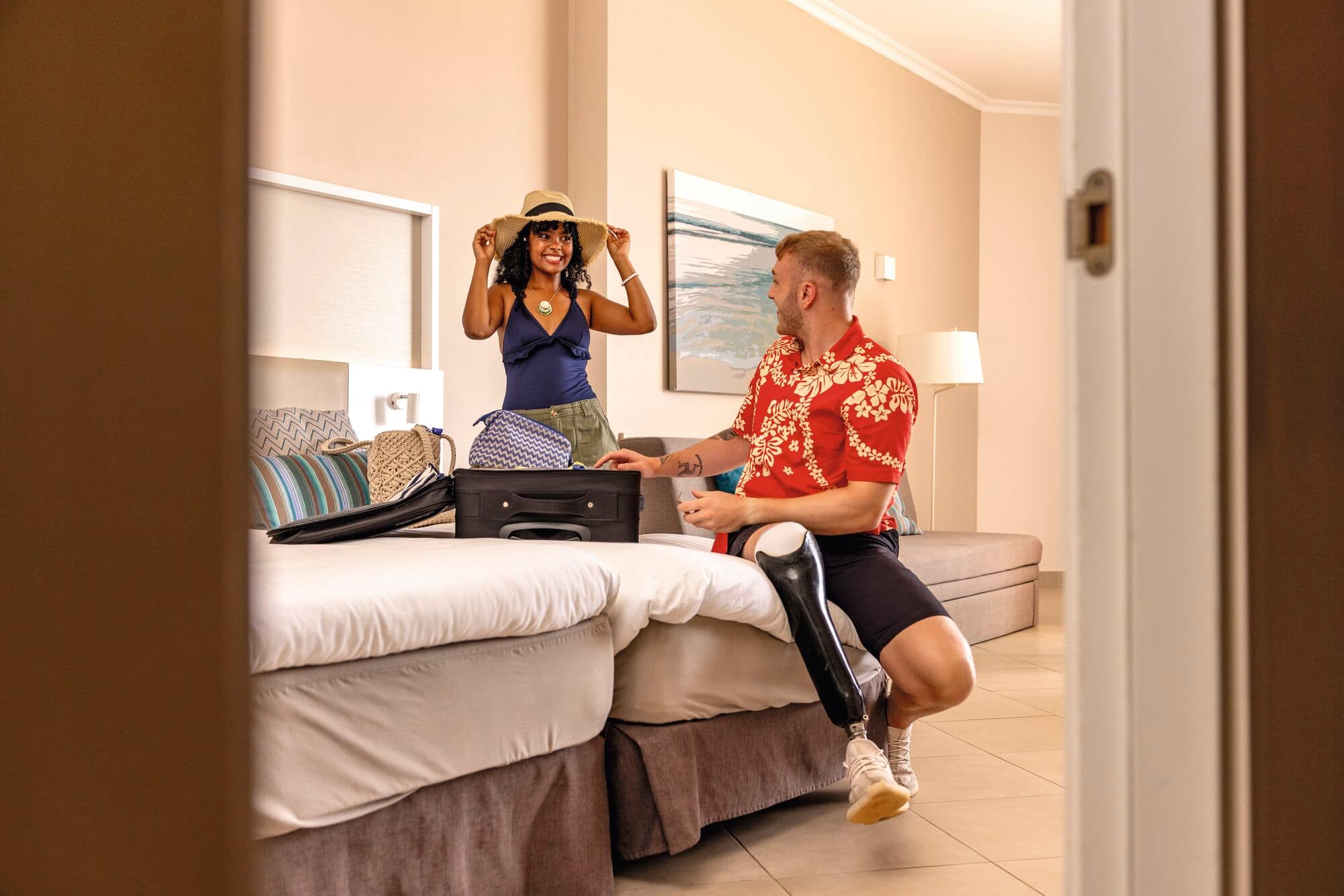 A couple smiling and unpacking suitcases in their hotel room.