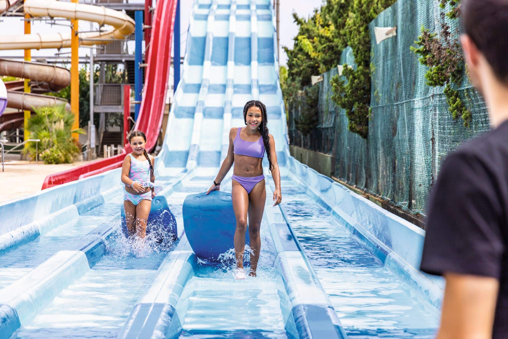 Two people sliding down a multi-lane water slide at a water park.