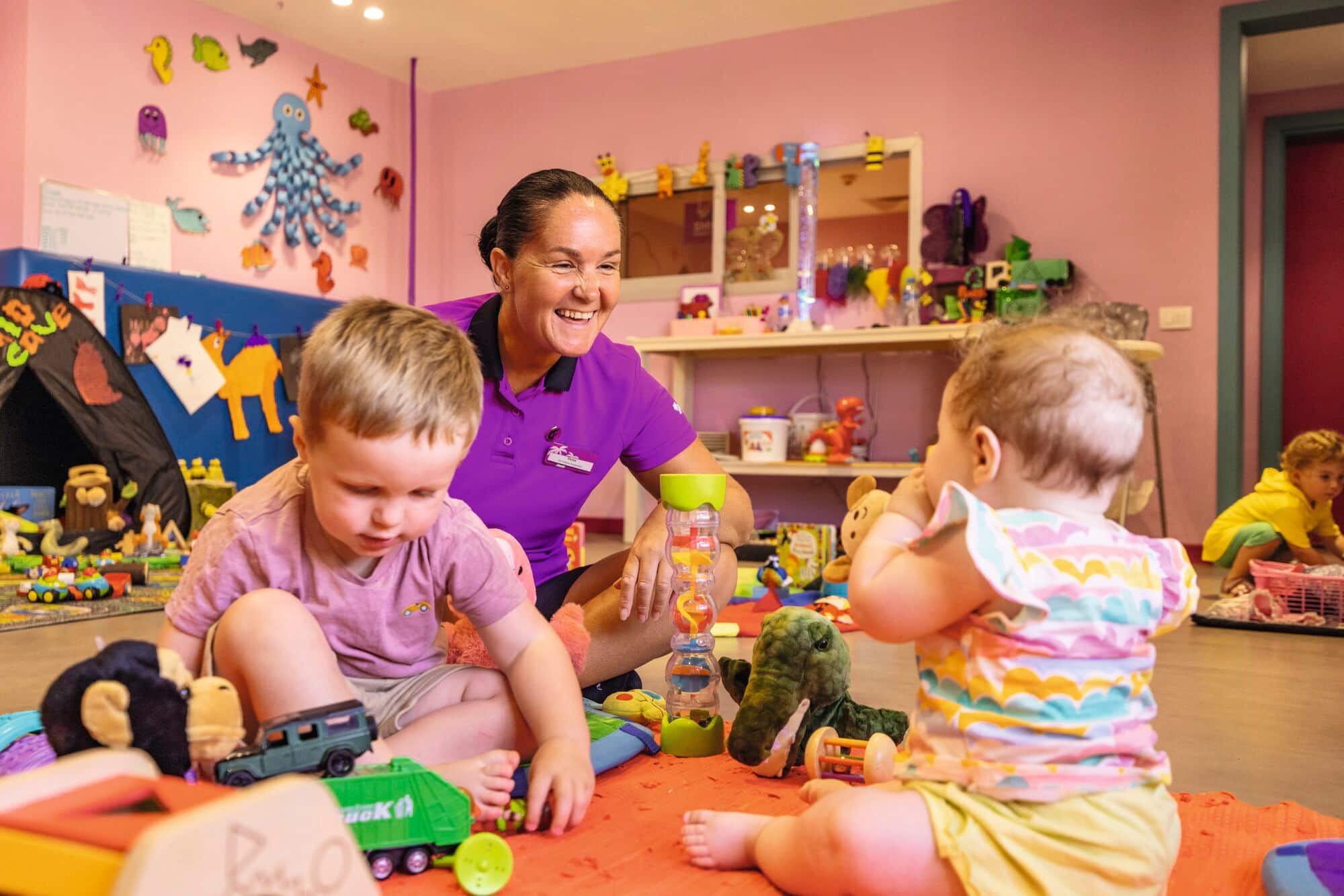 A woman smiling and playing with young children.