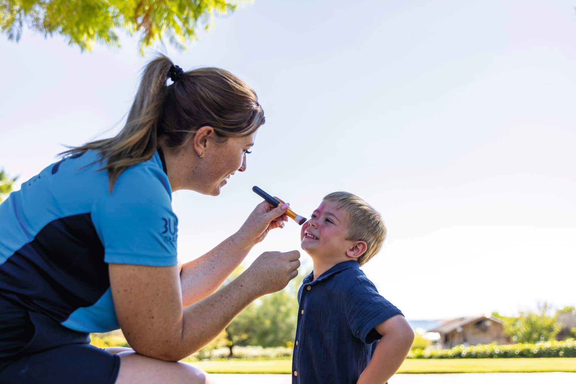 Kids club worker applying face paint on young child.