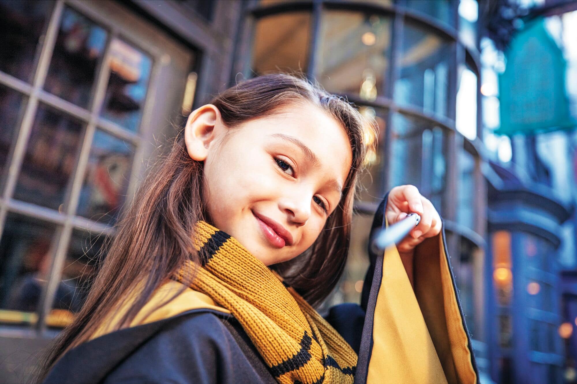 A girl in a black and yellow scarf, holding a wand.