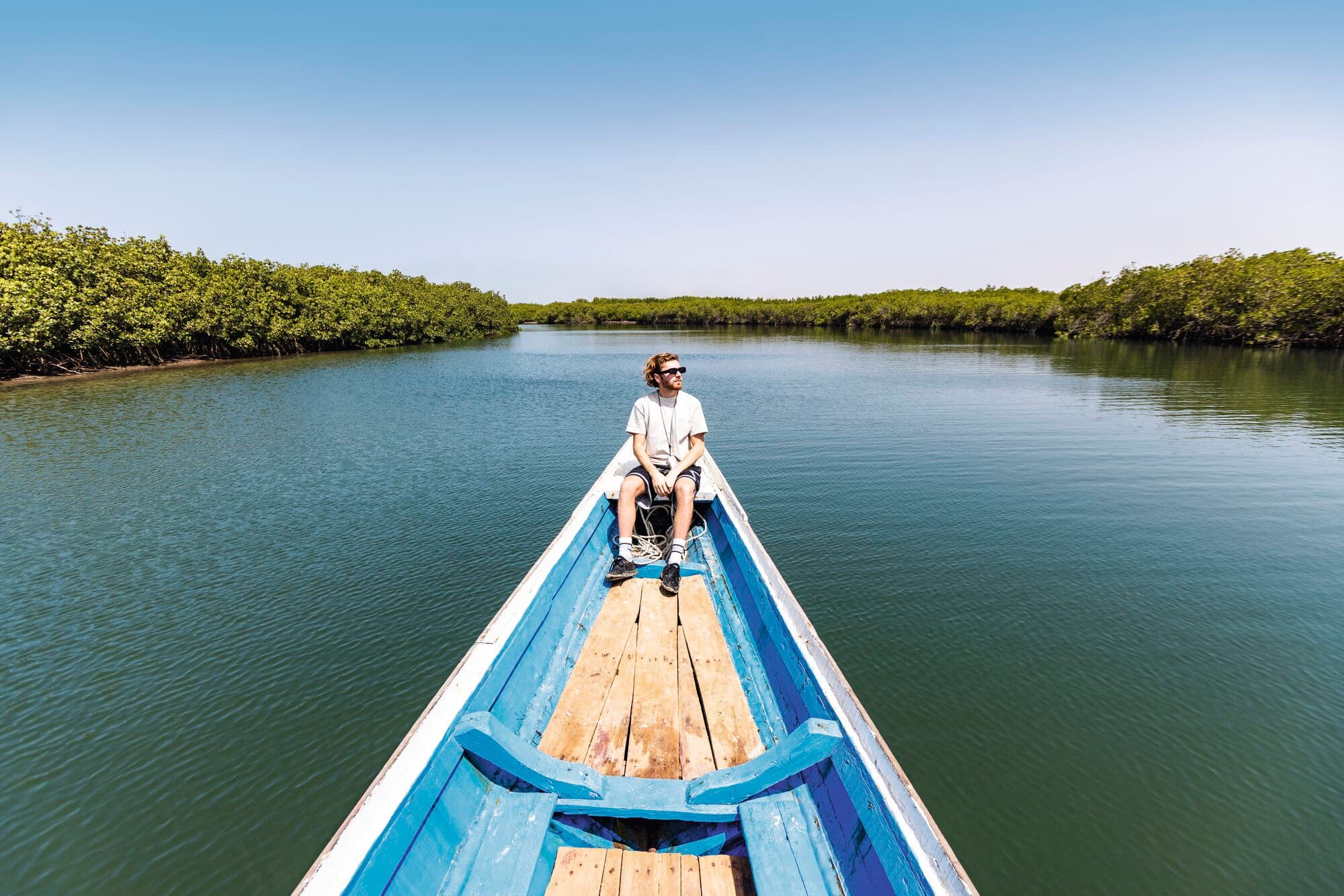 A man on a longboat, drifting down a river in Saloum Delta National Park, Senegal.