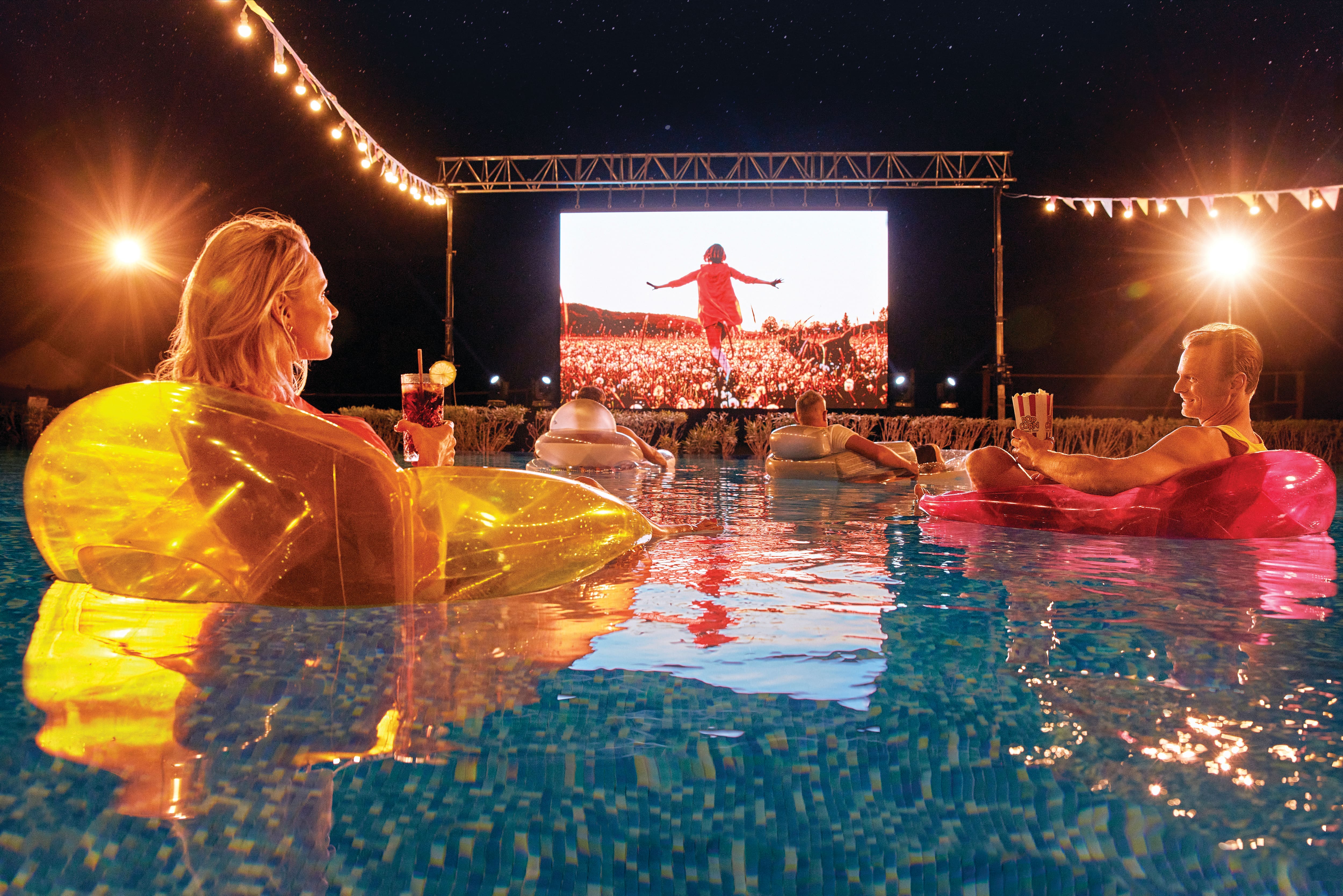 Four people on inflatables watching an outdoor movie from the pool.
