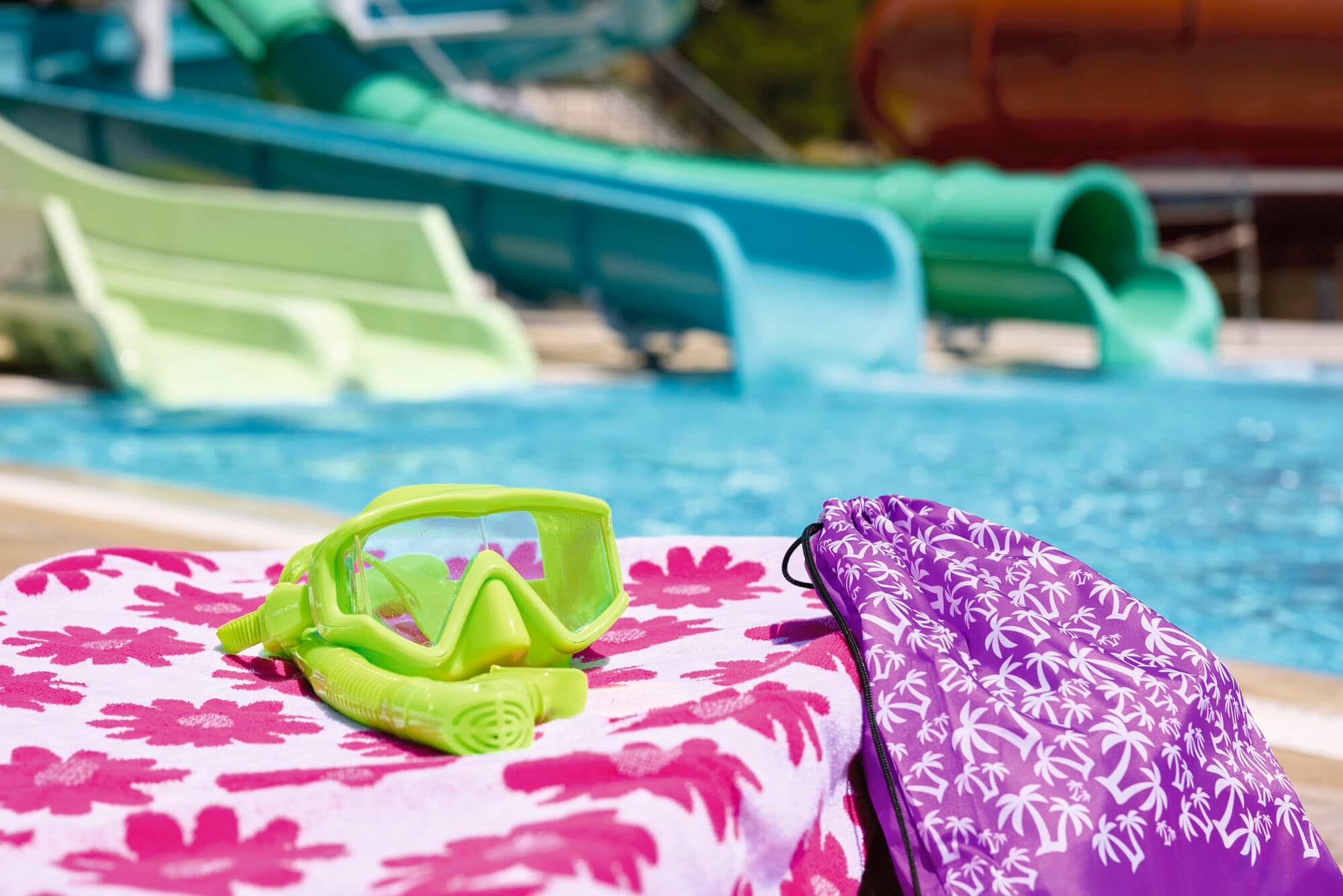 A pair of swimming goggles and a towel next to a pool.