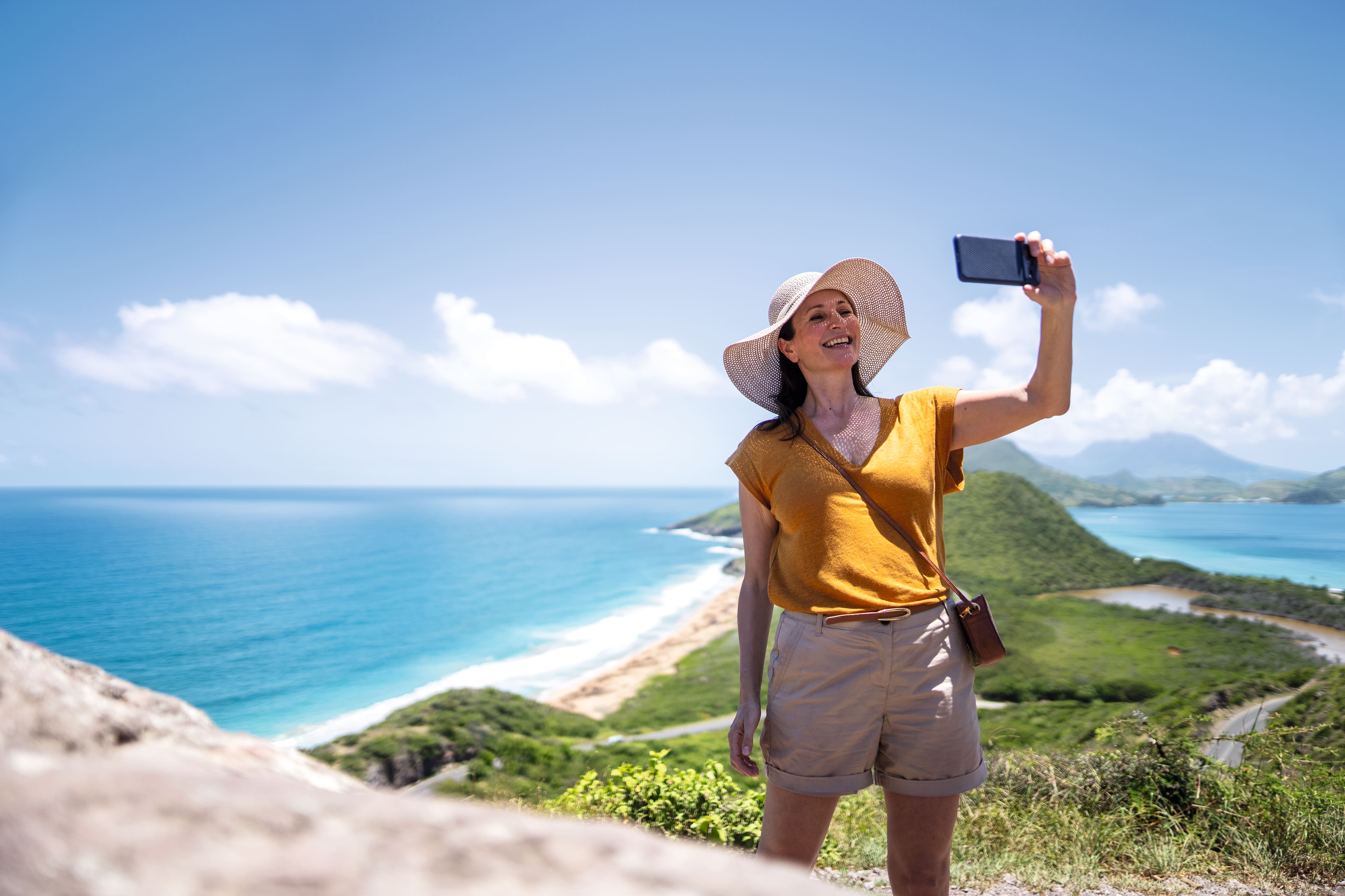 A woman in a sunhat taking a selfie in front of a green peninsula.