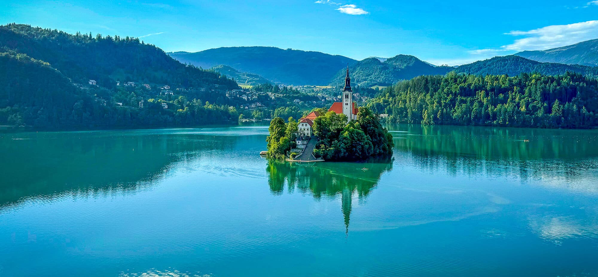 An island with a church on it in the middle of Lake Bled in Slovenia, seen from the shore. 