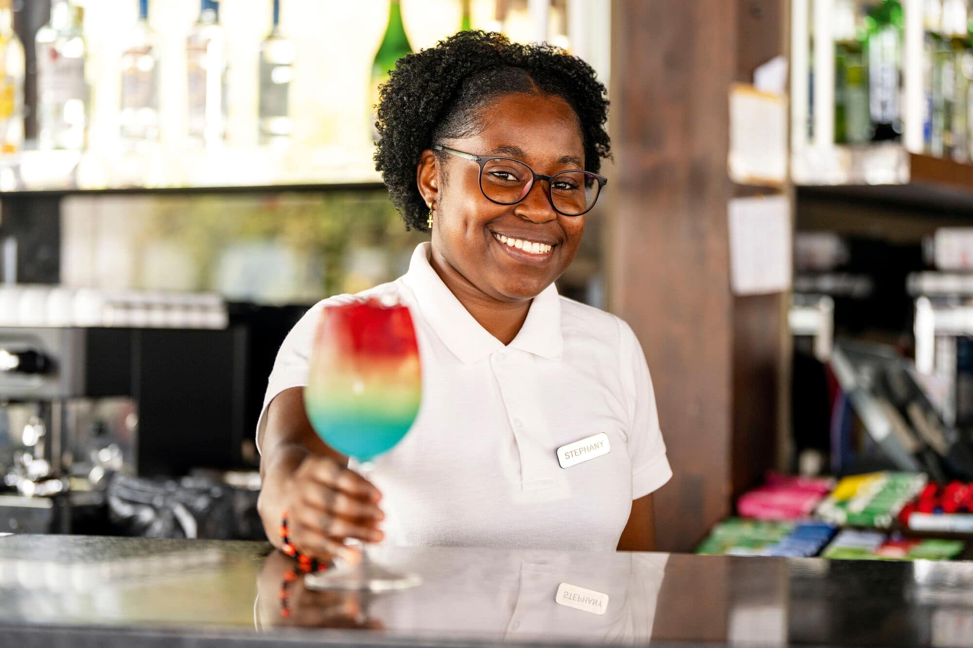 Bartender smiling and holding a colourful cocktail.