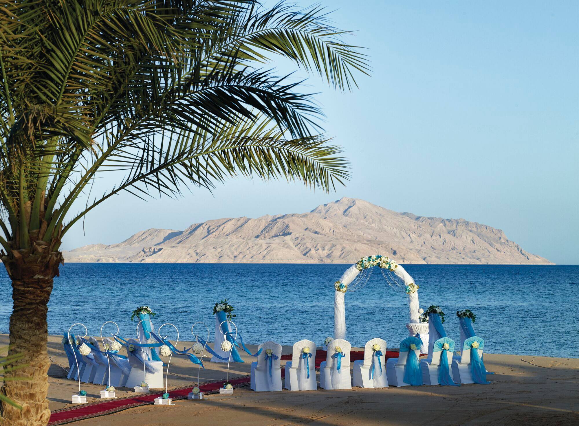 A beach wedding ceremony set-up with a wedding arch right by the water, looking out to an island.