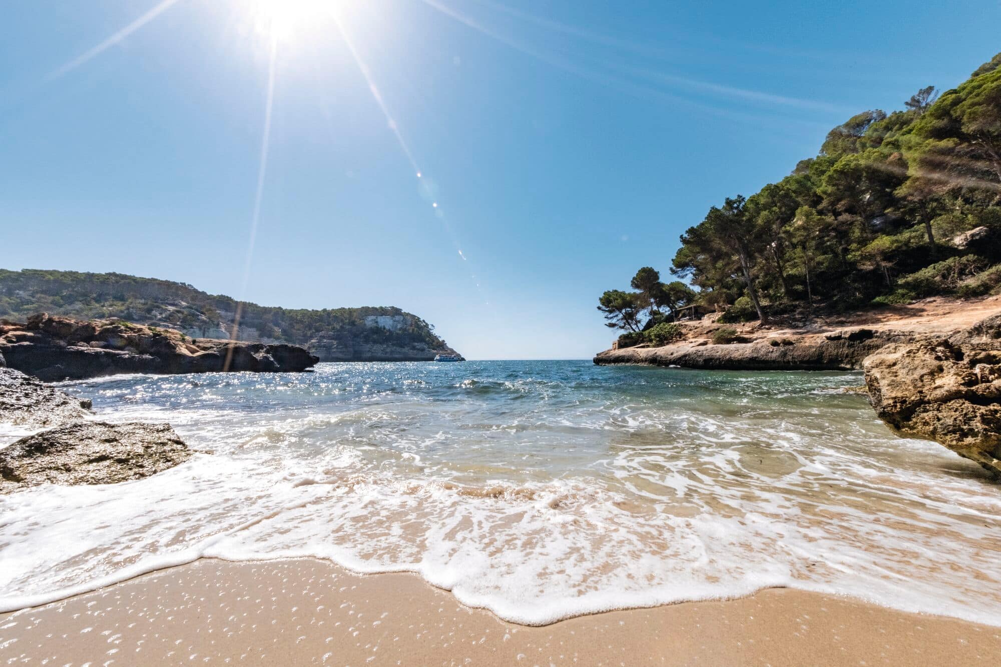 A secluded Mediterranean cove with turquoise water meeting a sandy beach.