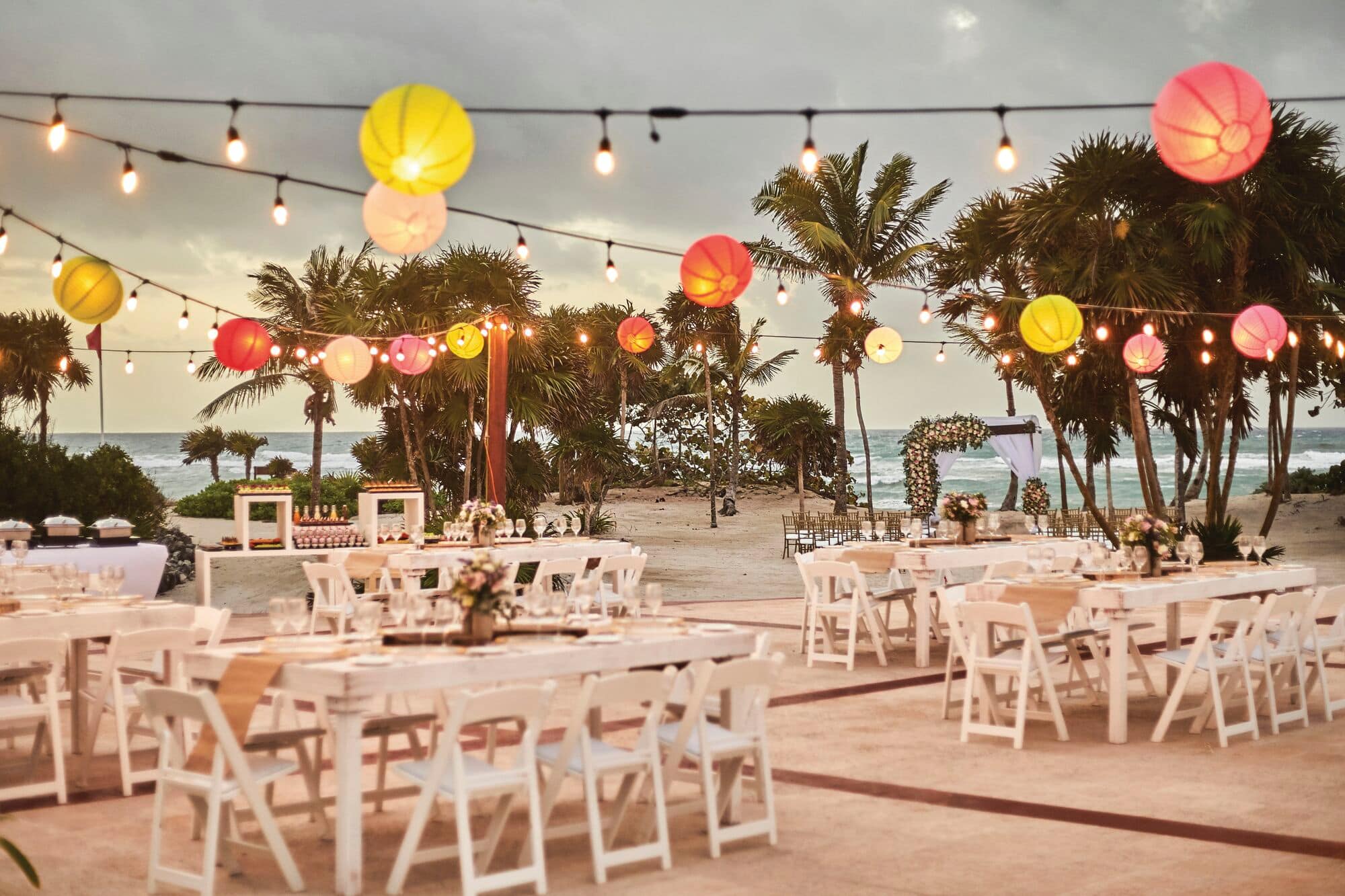 A colourful beach wedding ceremony set-up with lanterns, palm trees and seaside views.