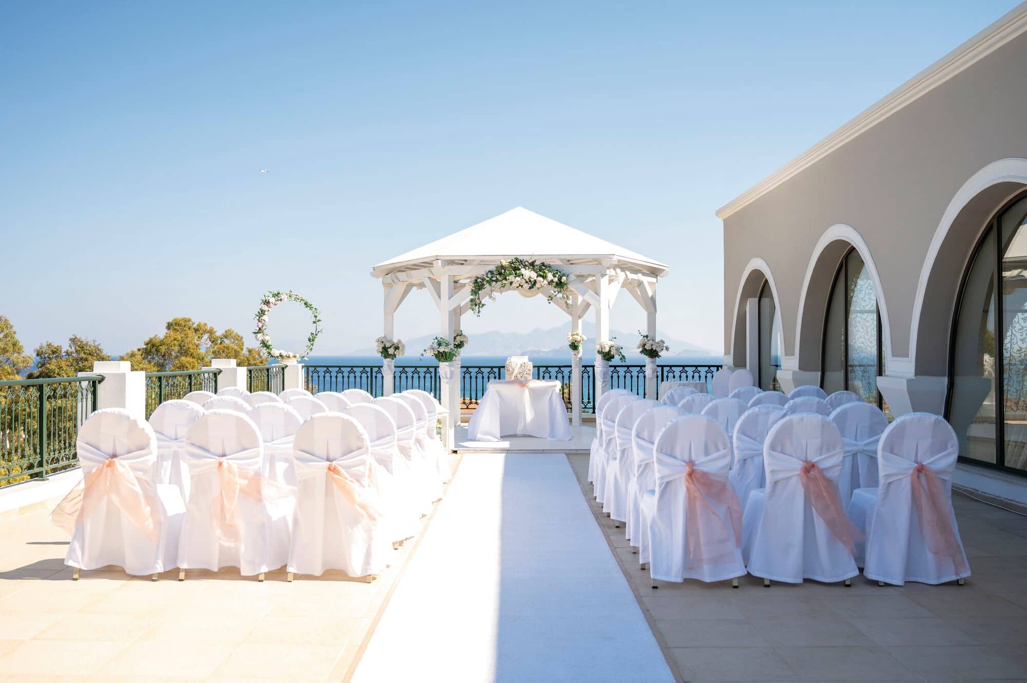 An outdoor wedding ceremony setup with white chairs and a gazebo overlooking the sea.