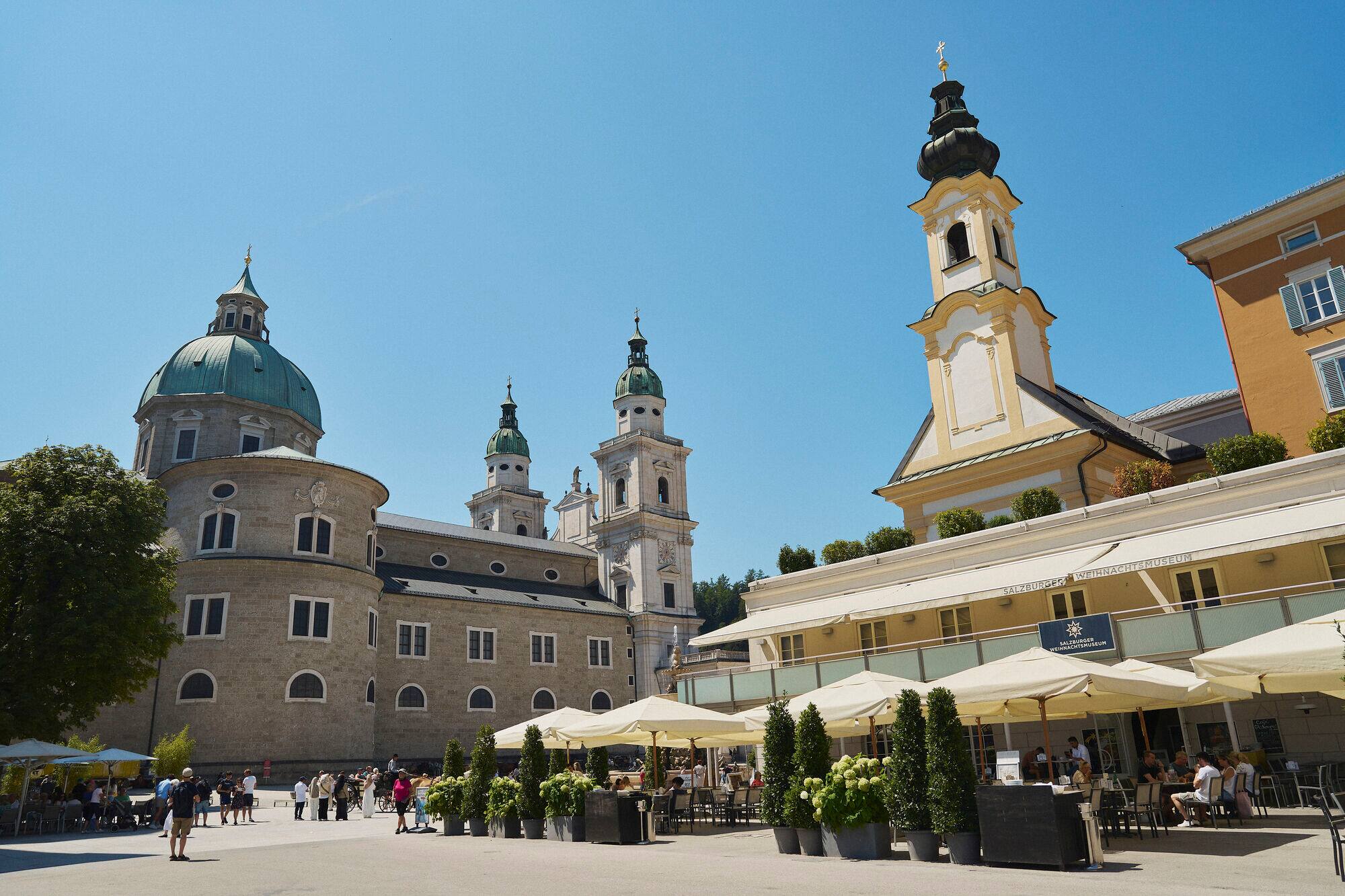 Motzartplatz in Salzburg. A square with a church and cafe with an outdoor area with a canopy. 