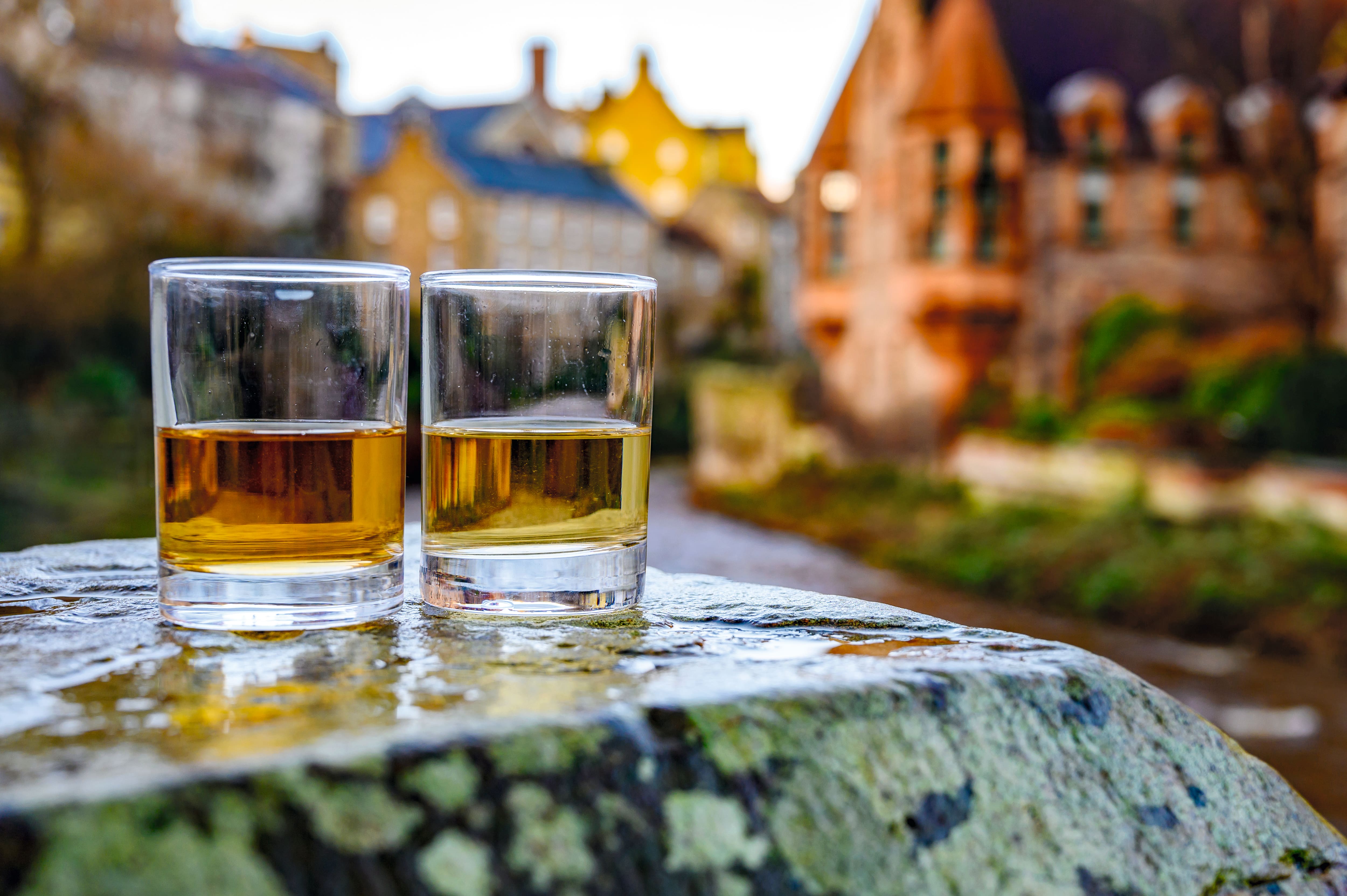 Two glasses of whiskey on a table in a Scottish setting.