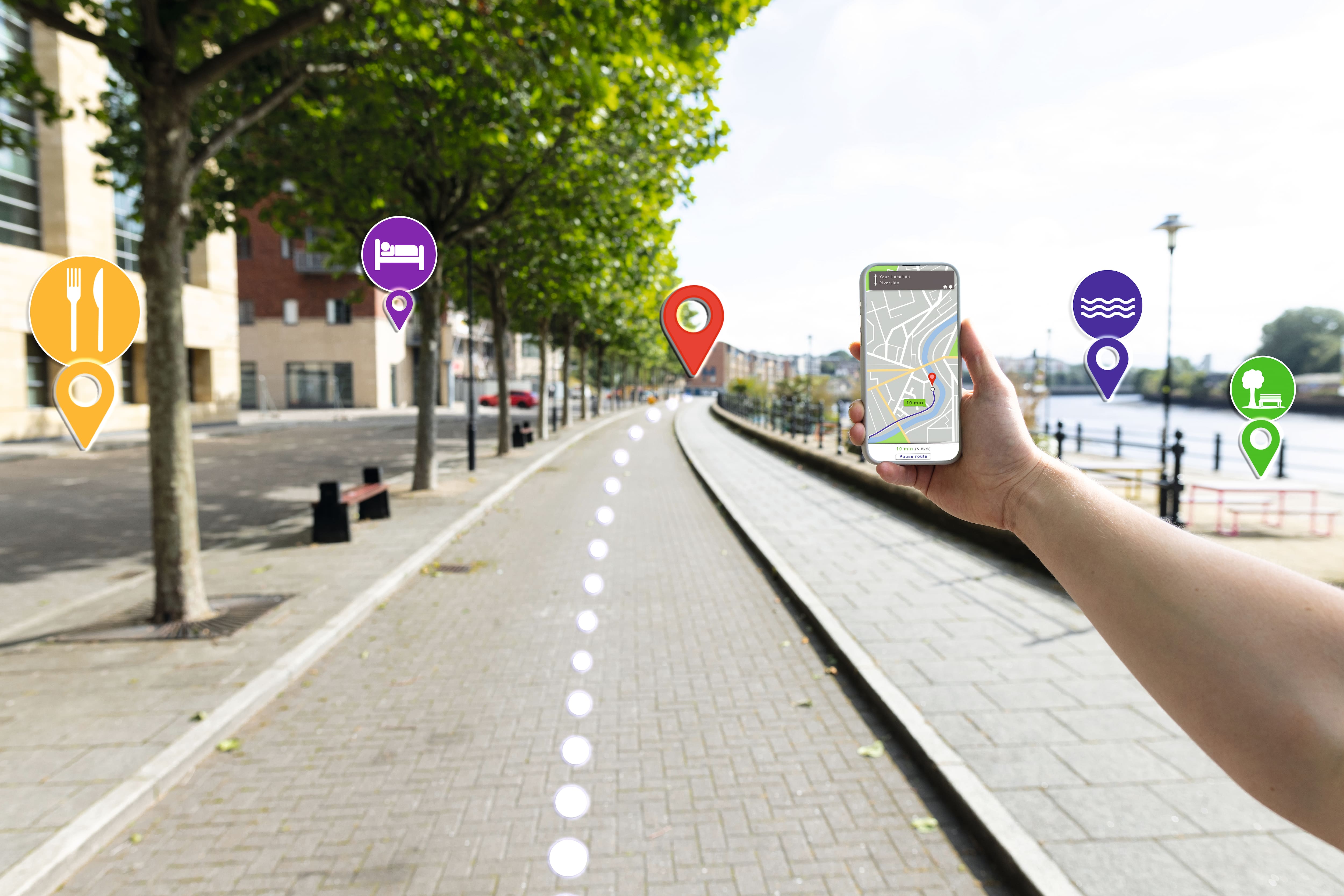 Person holding mobile phone with map on screen walking down a street.