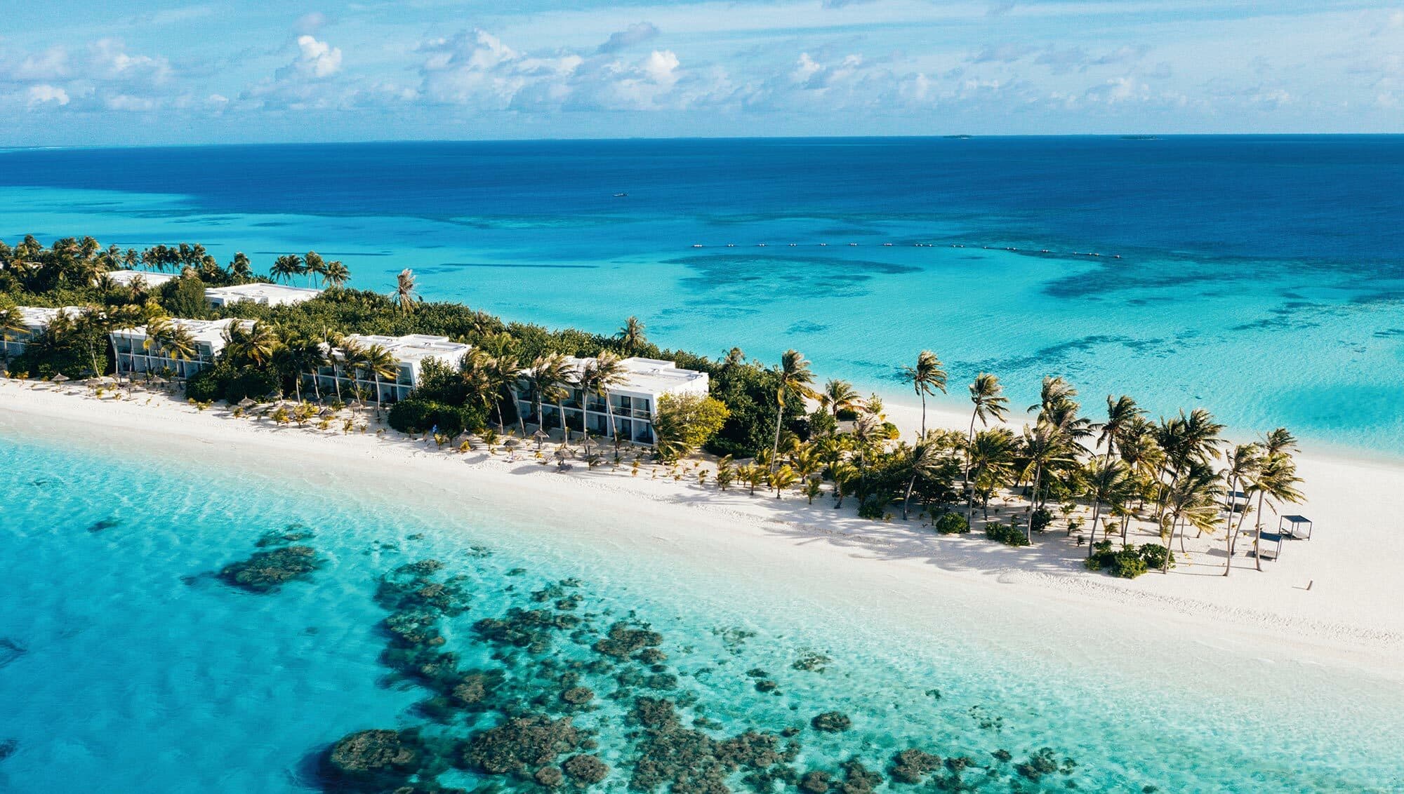An aerial view of Riu Atoll on a thin strip of sand amidst a sprawling blue sea.