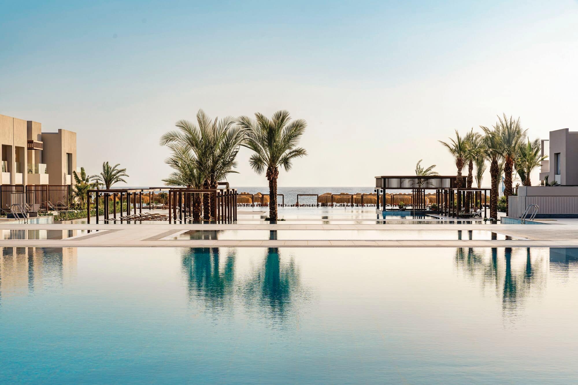 A view of a hotel pool, with palm trees reflecting in the water.