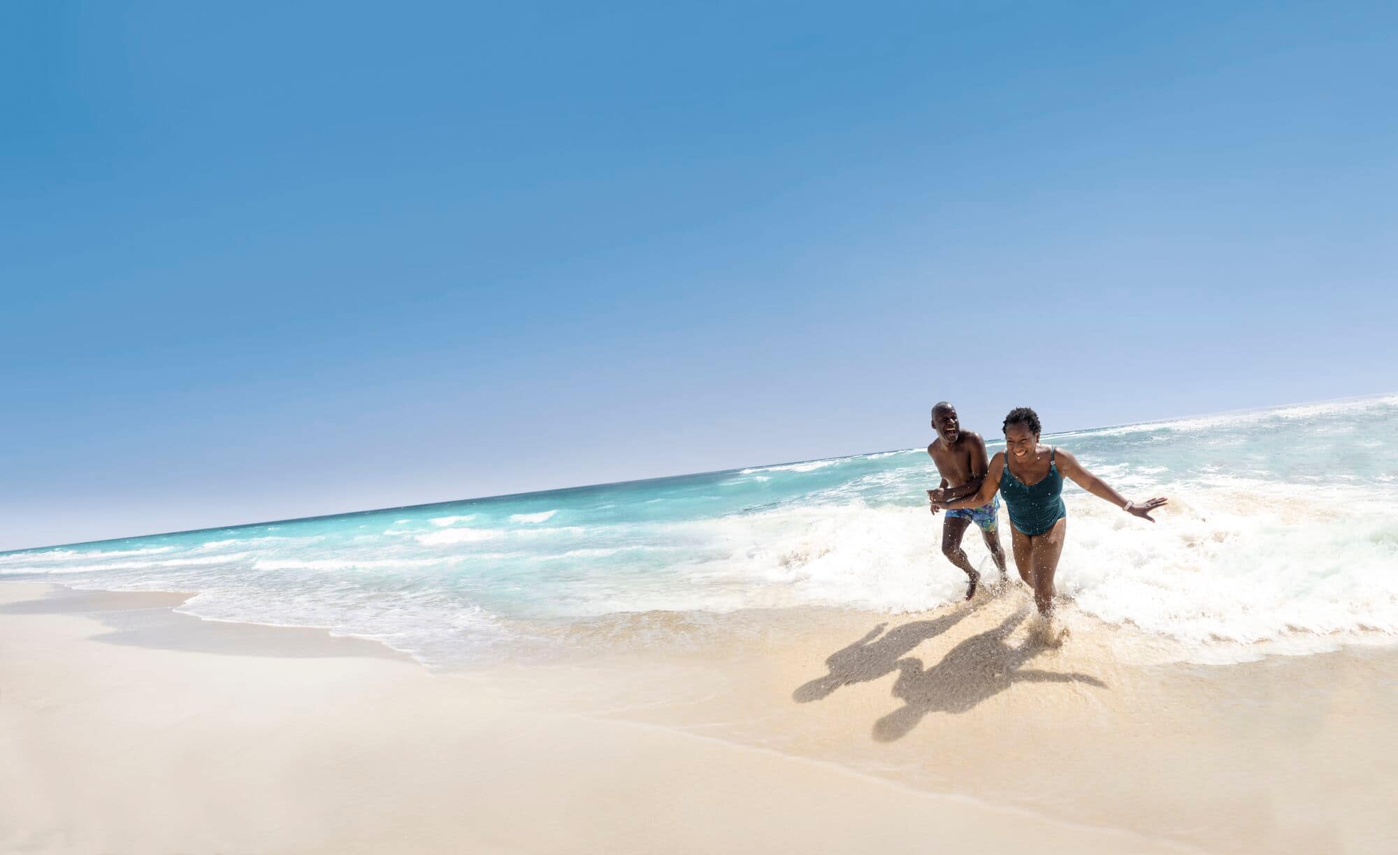A couple run laughing out of the sea.