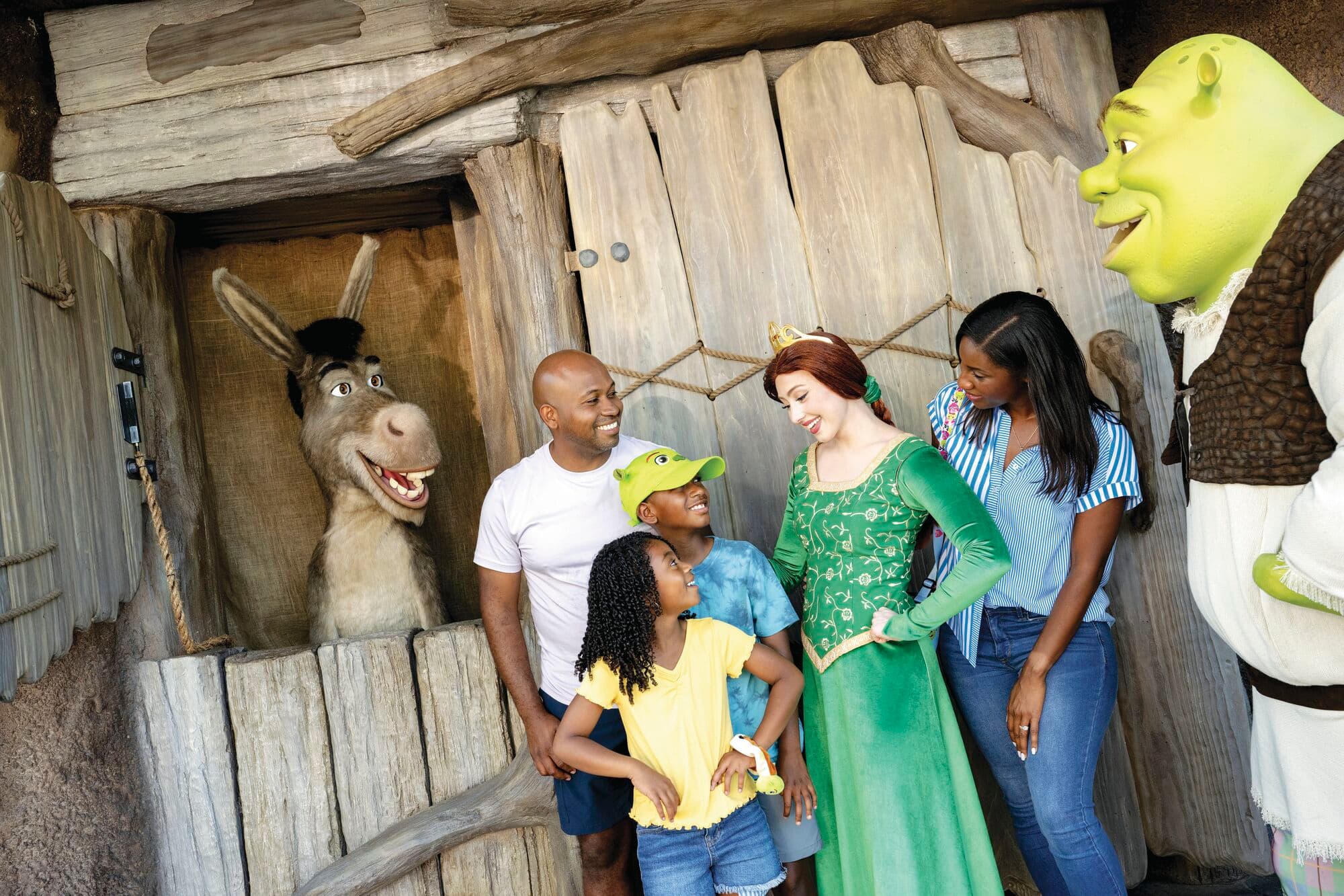 A smiling family stand with Shrek, Fiona and Donkey.