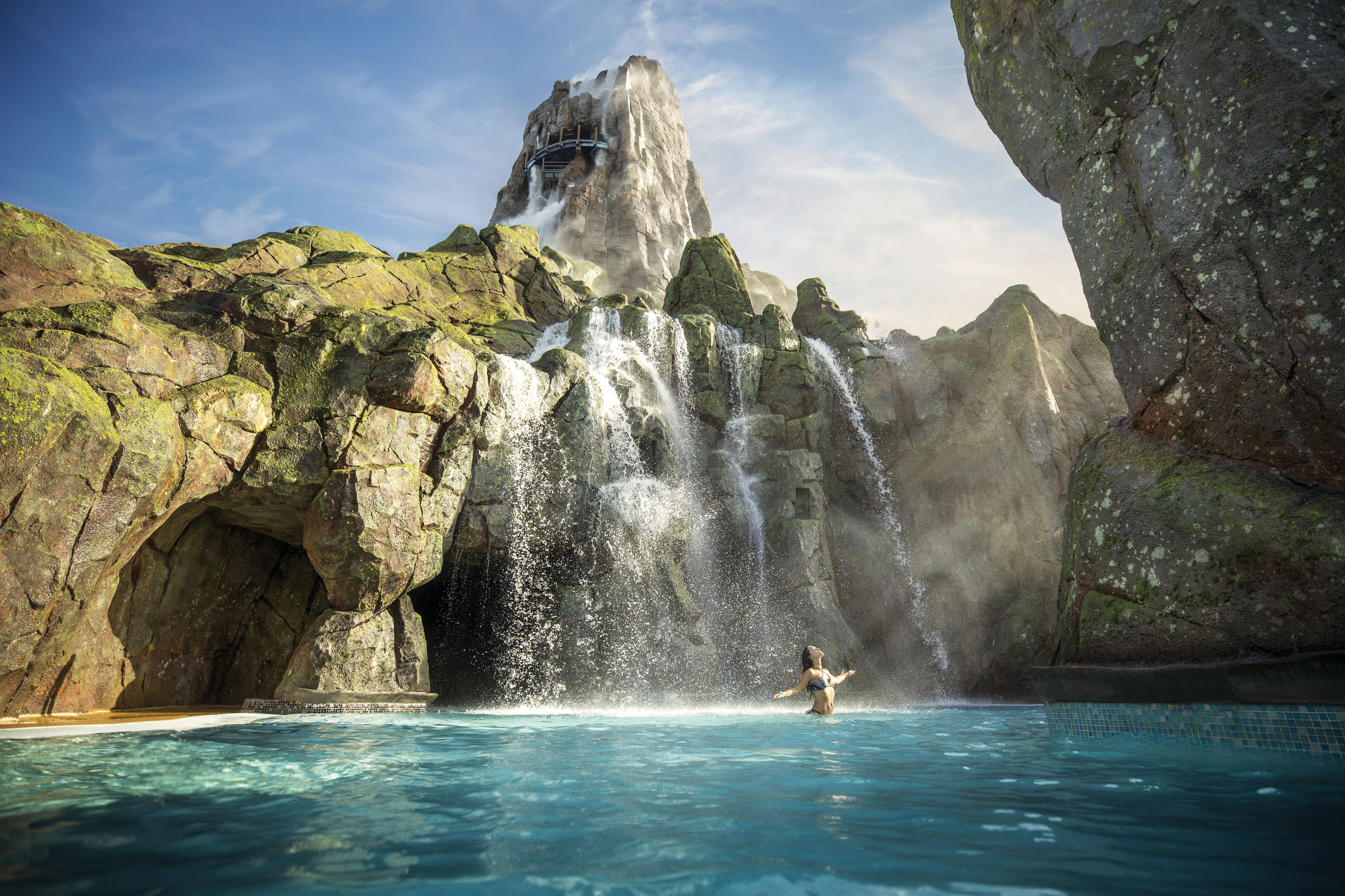 Girl in water with volcano waterfall in background.