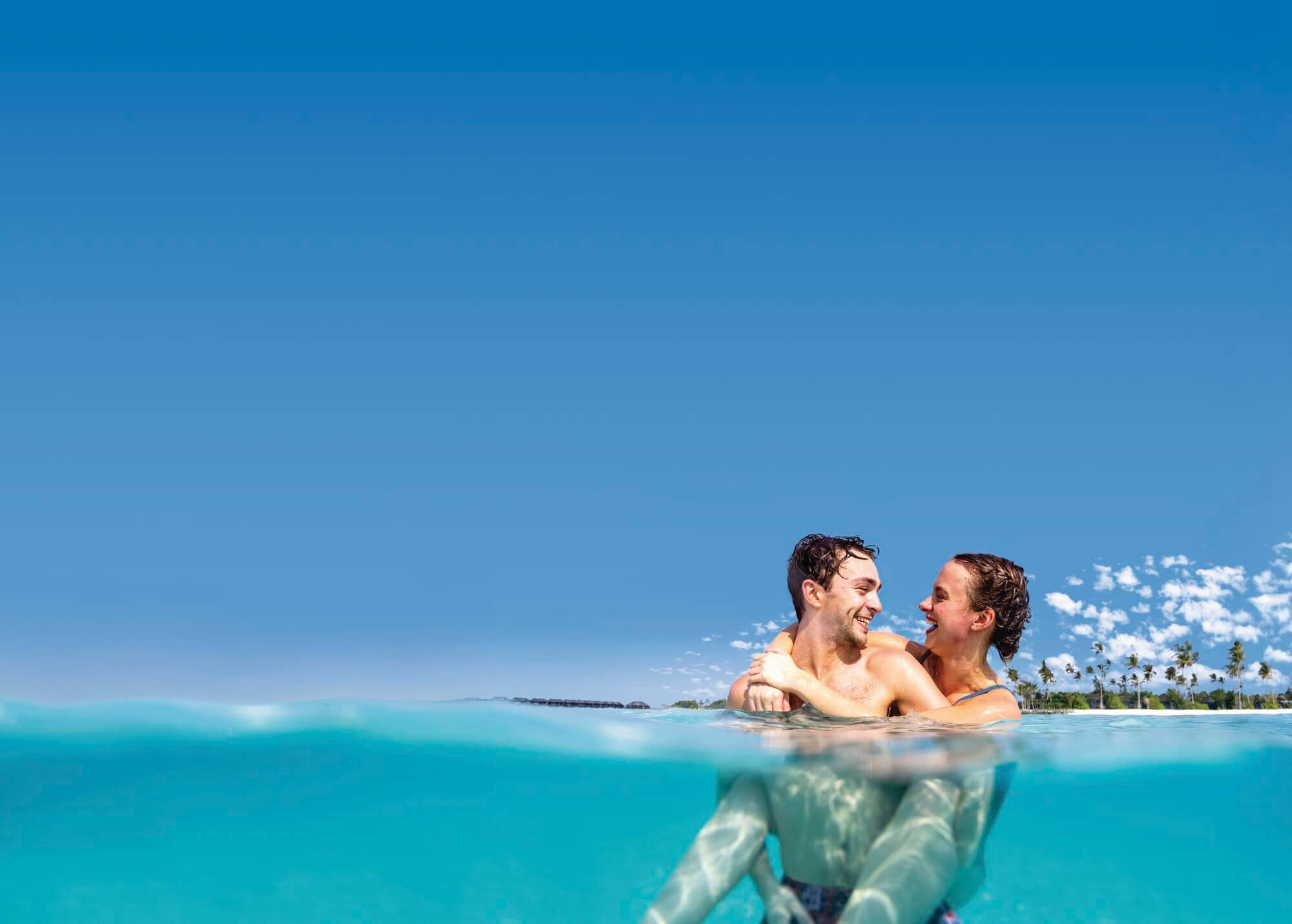 A couple in clear tropical water with palm trees in the background.