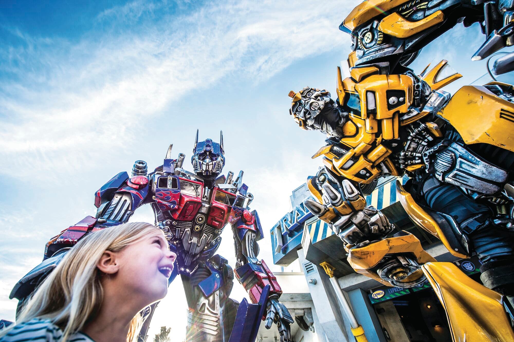 A child stands in front of two giant Transformers at Universal Studios Florida.