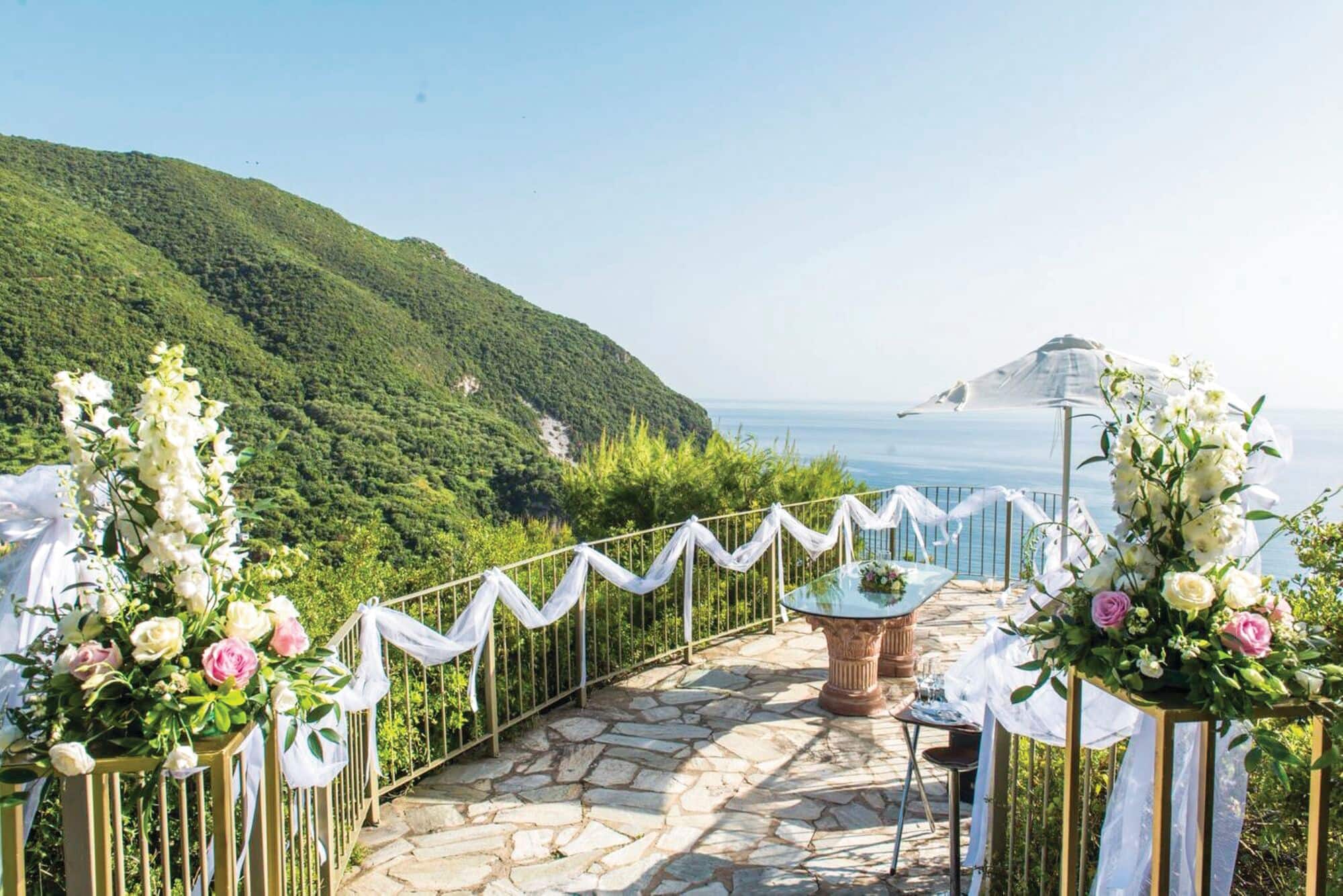 Outdoor wedding ceremony setup on a stone terrace overlooking a scenic coastline.