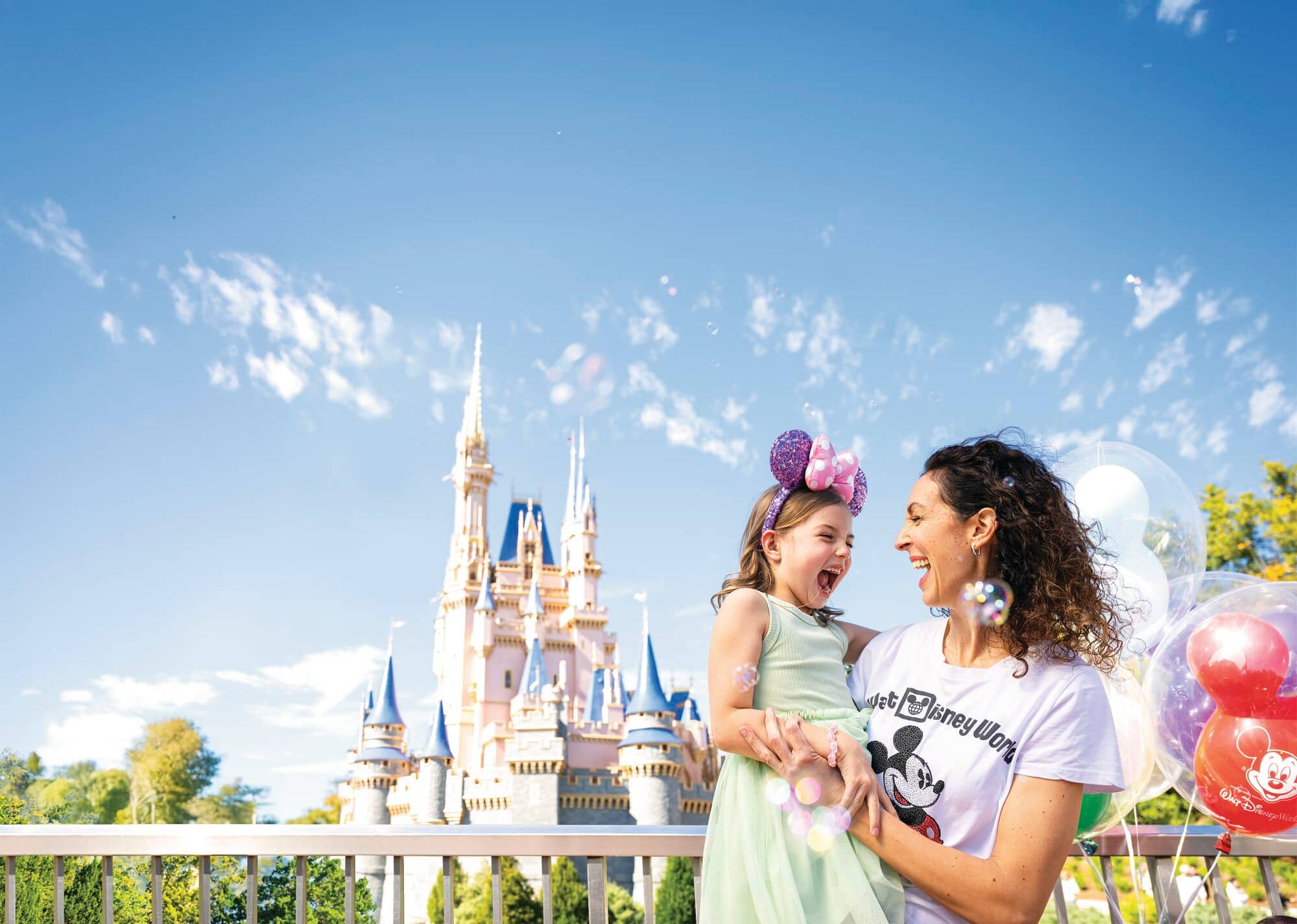 A family of two in front of the Cinderella Castle. Mickey Mouse themed balloons are in the foreground.