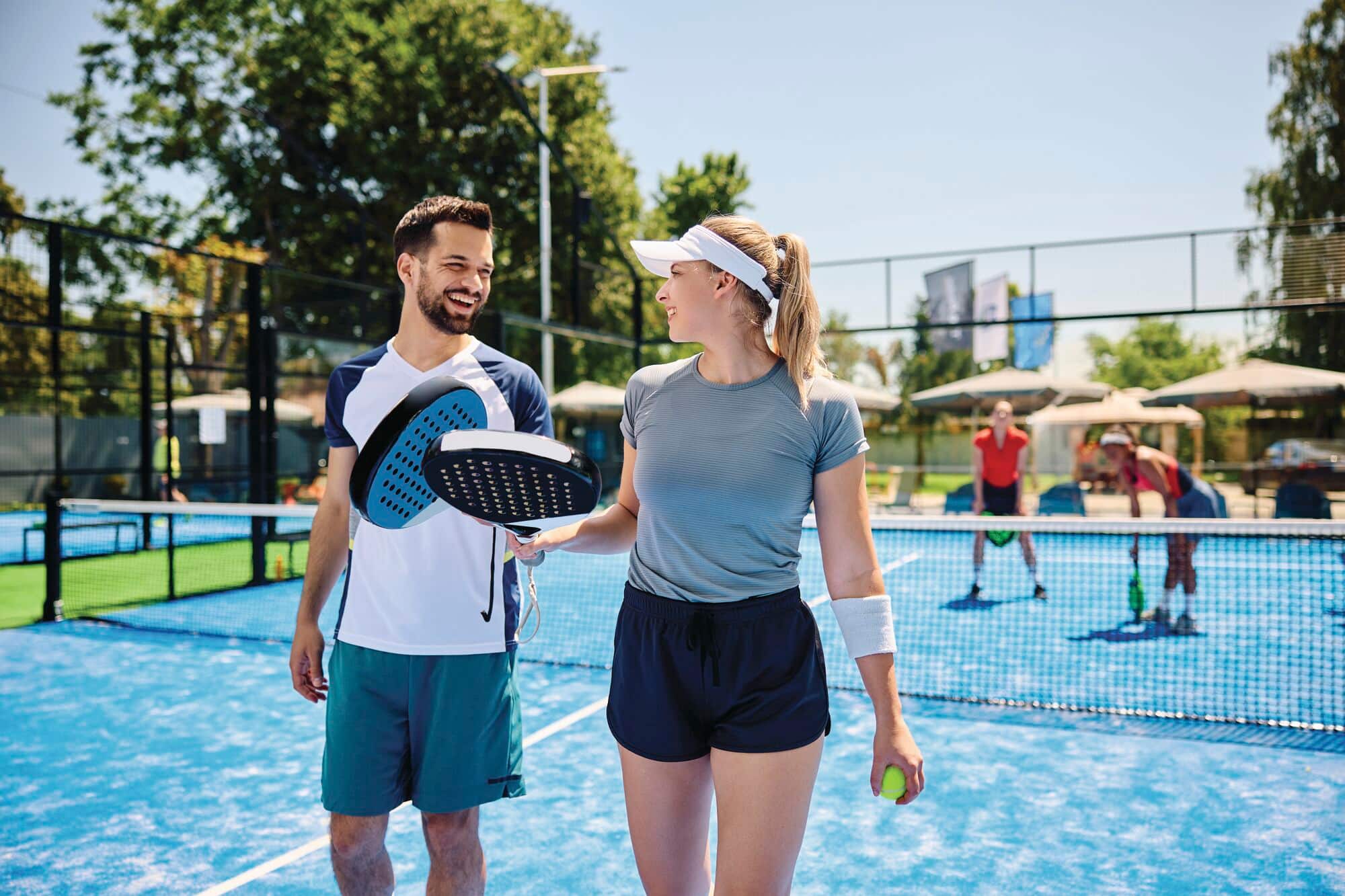 A couple talk while playing mixed doubles in paddle tennis. Image shown for illustrative purposes only.