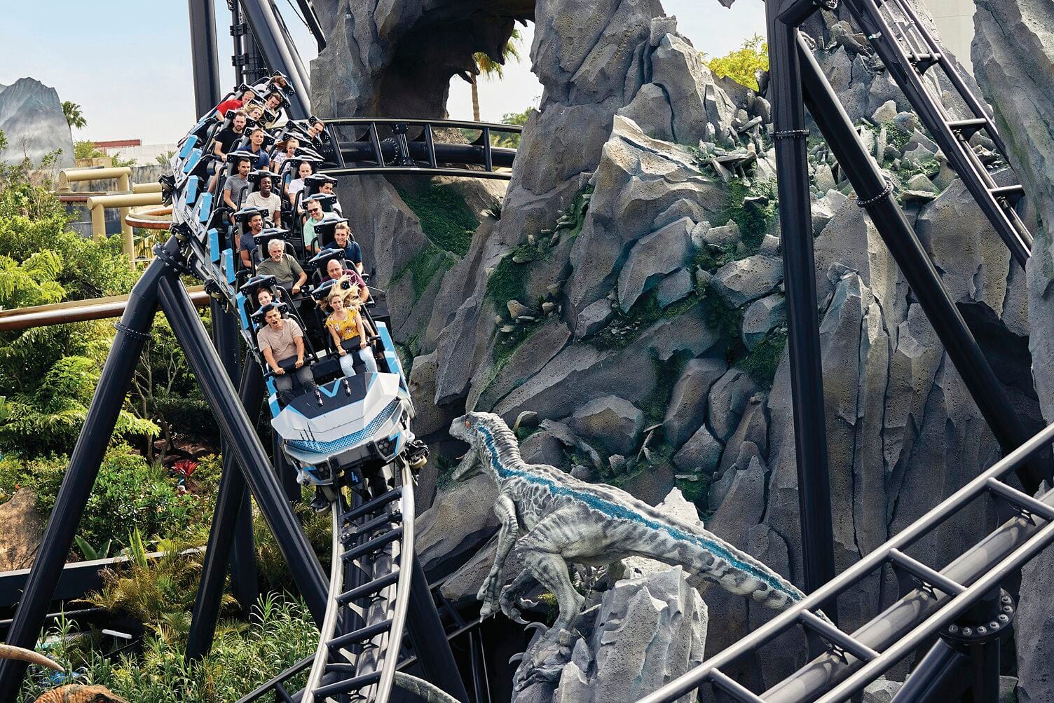Thrill-seekers race down a twisting coaster past a fierce raptor in a rocky jungle setting.
