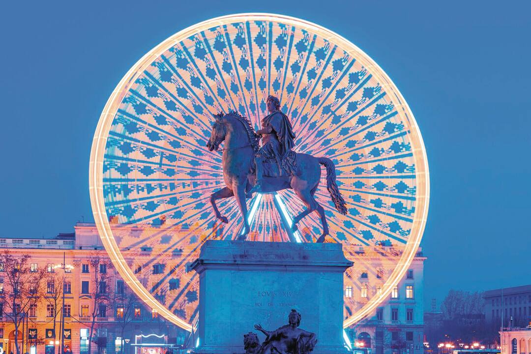 The statue of King Louis XIV in Place Bellecour, with a lit Ferris wheel behind