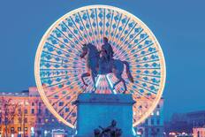 The statue of King Louis XIV in Place Bellecour, with a lit Ferris wheel behind