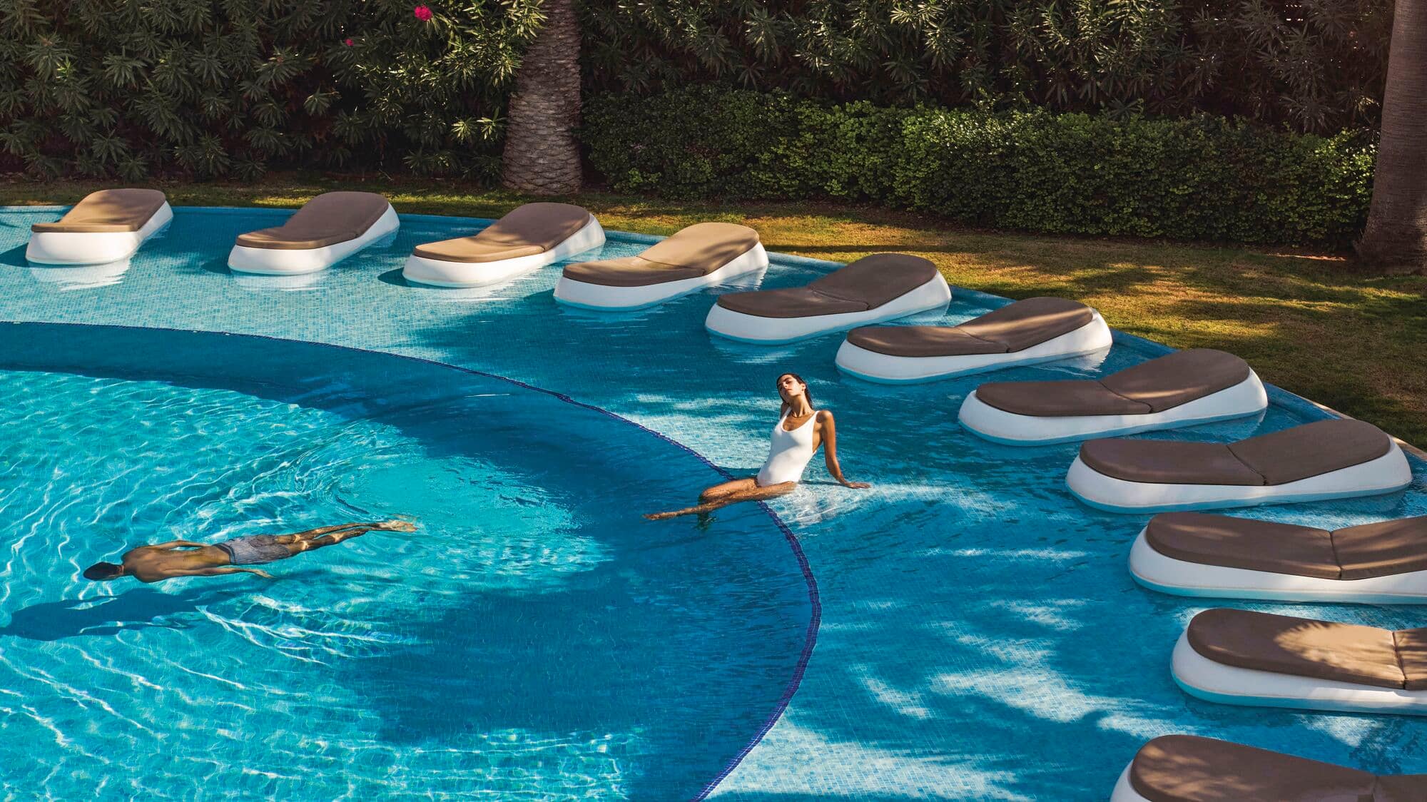 Two people swimming in a pool with in-water sunbeds.