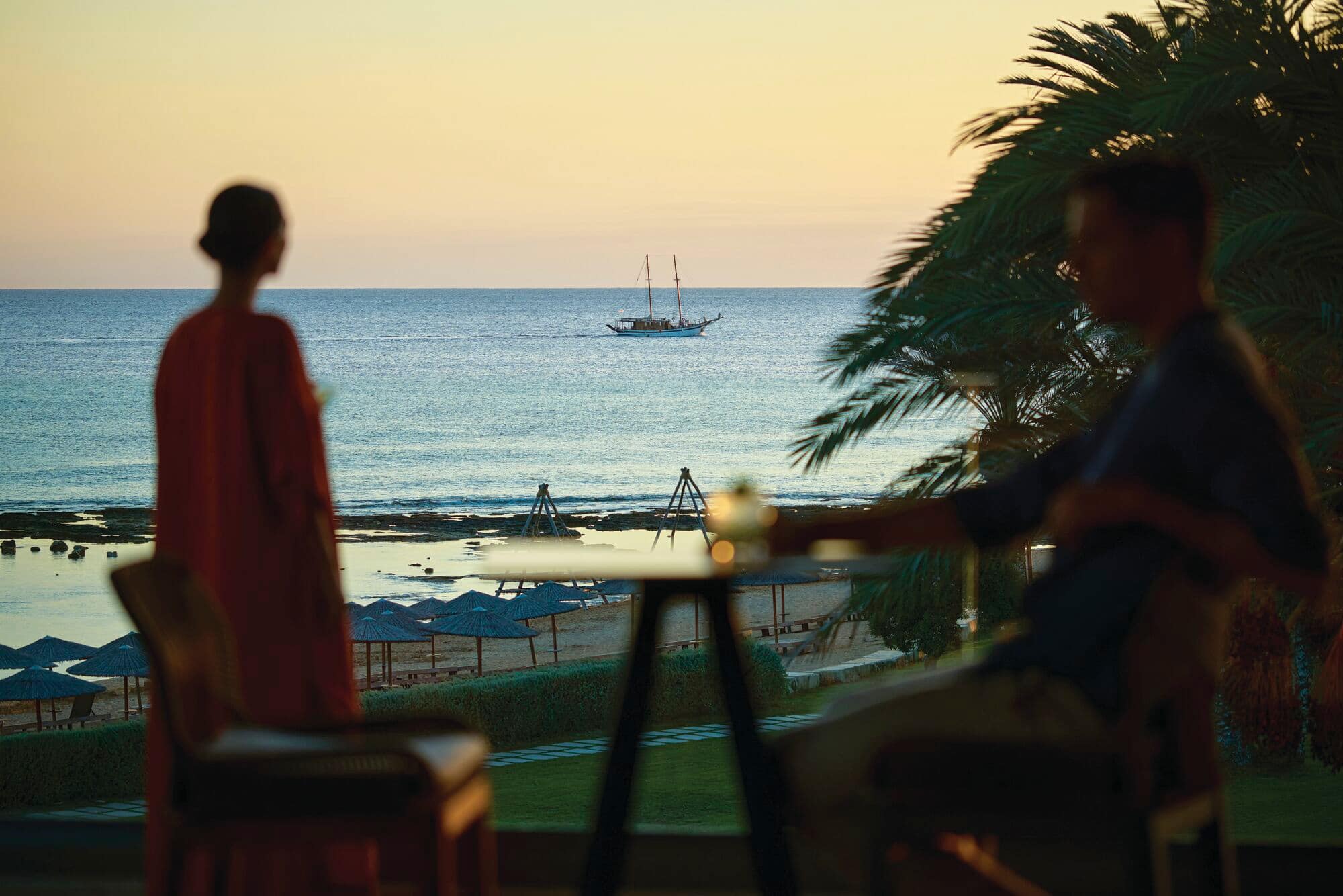 A couple at an outdoor bar, looking out to sea.