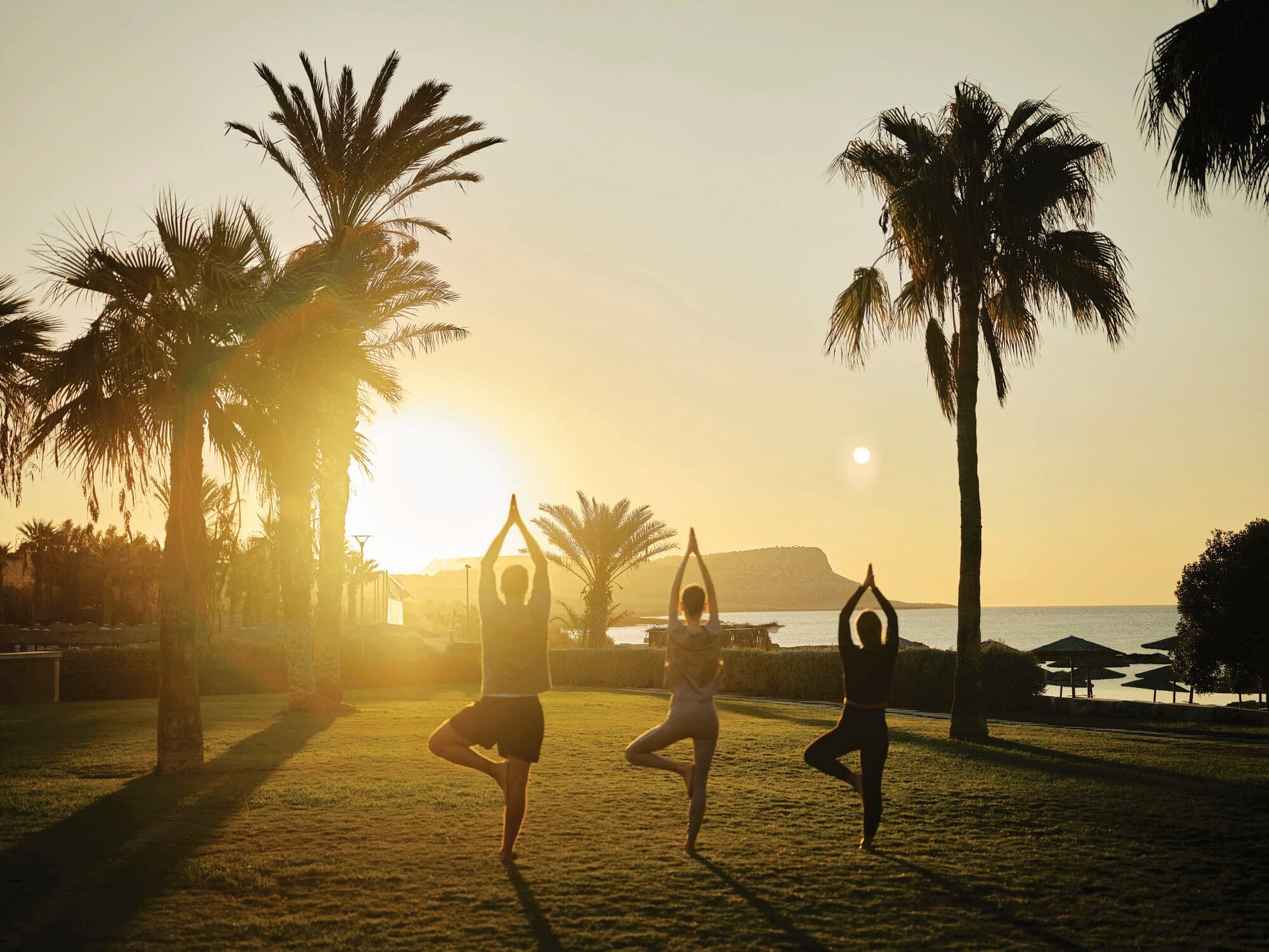 Three people doing yoga at sunset.