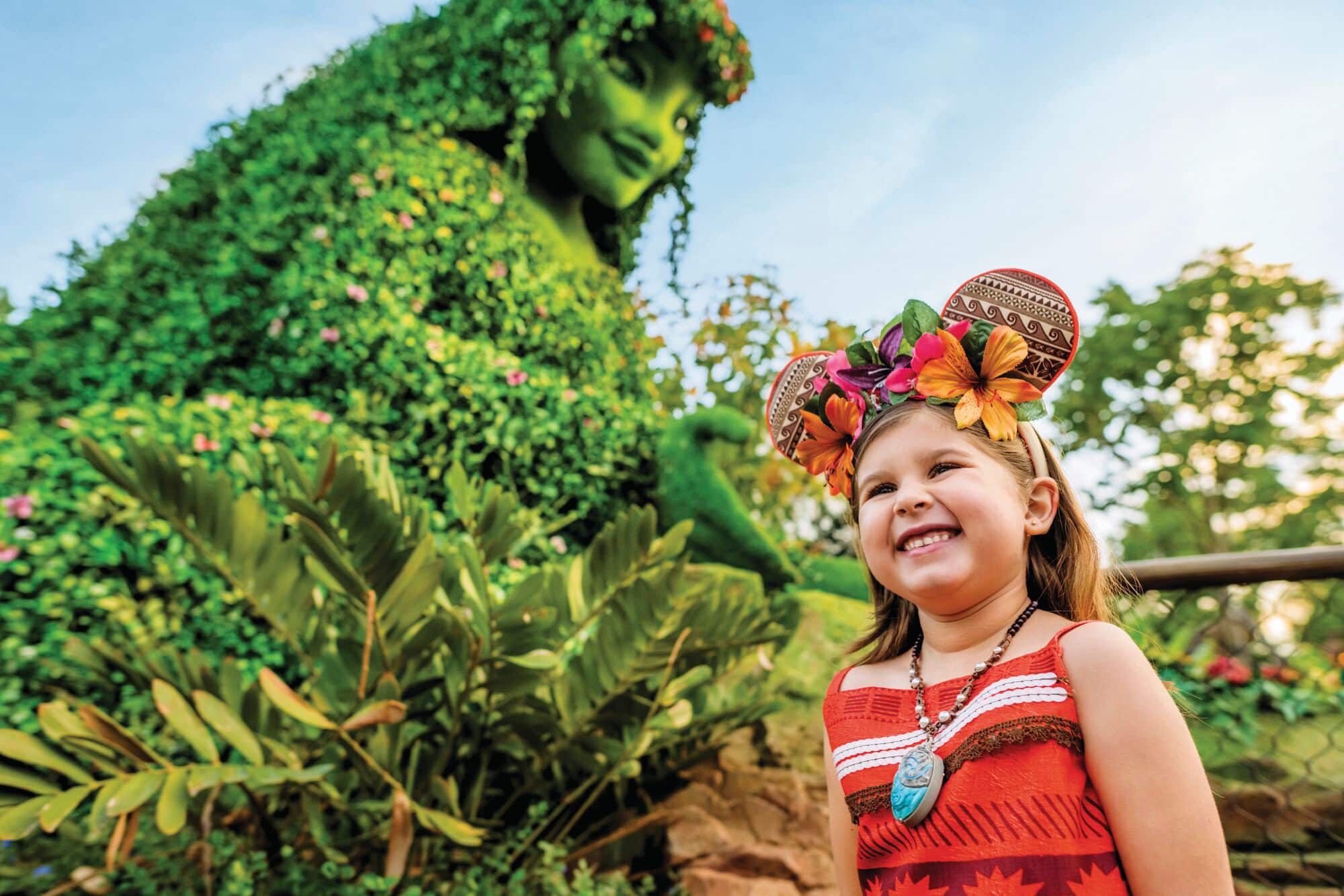A child in front of a Moana shaped hedge.