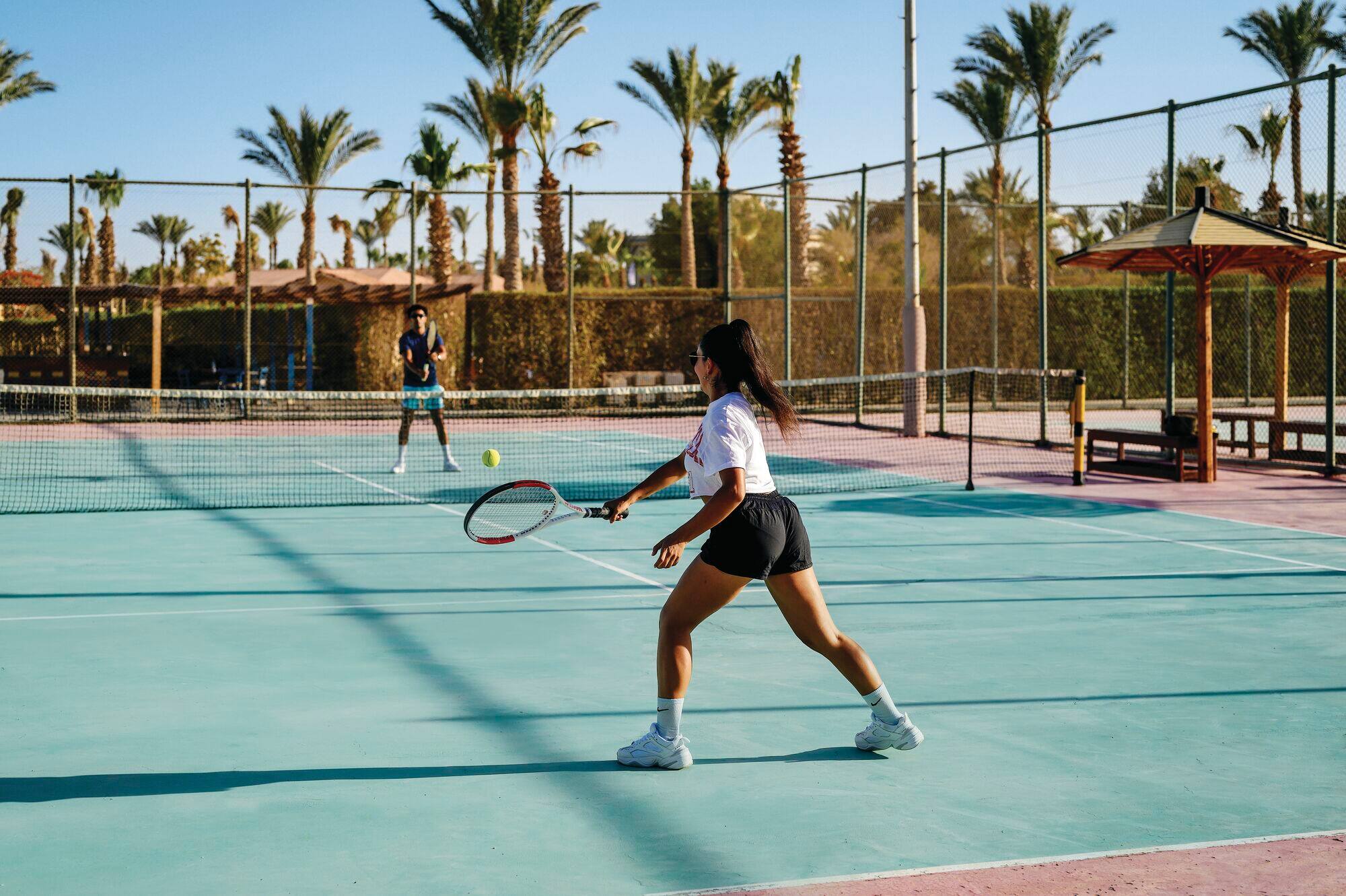 A man and woman play tennis on a sunny court.