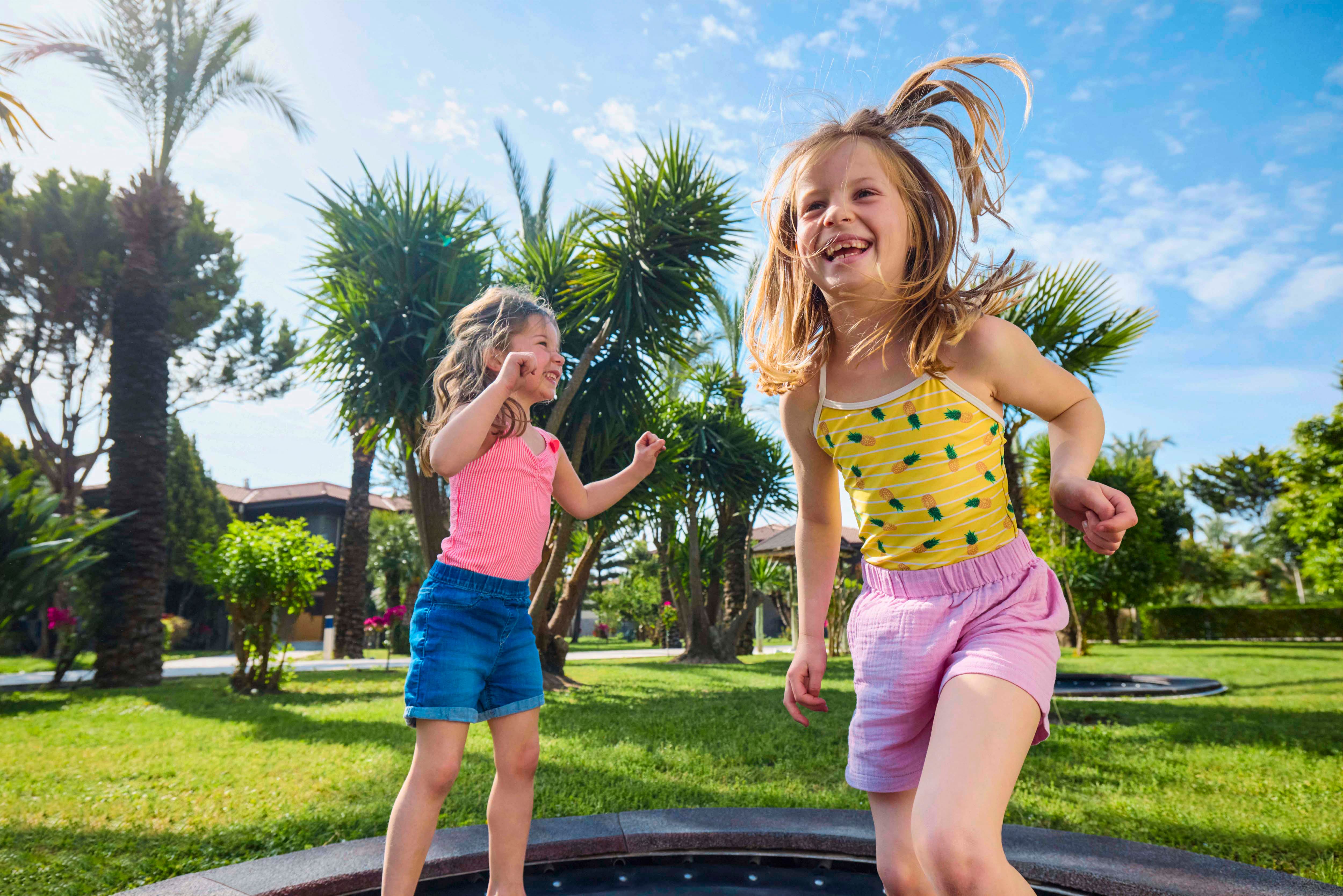 Two children jumping on a trampoline in green hotel gardens.
