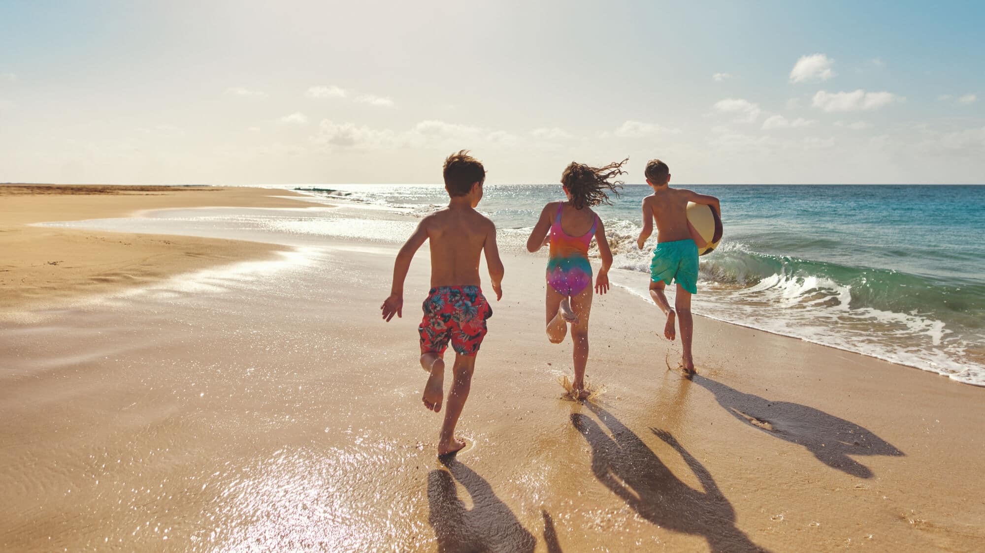 Three children running down a beach