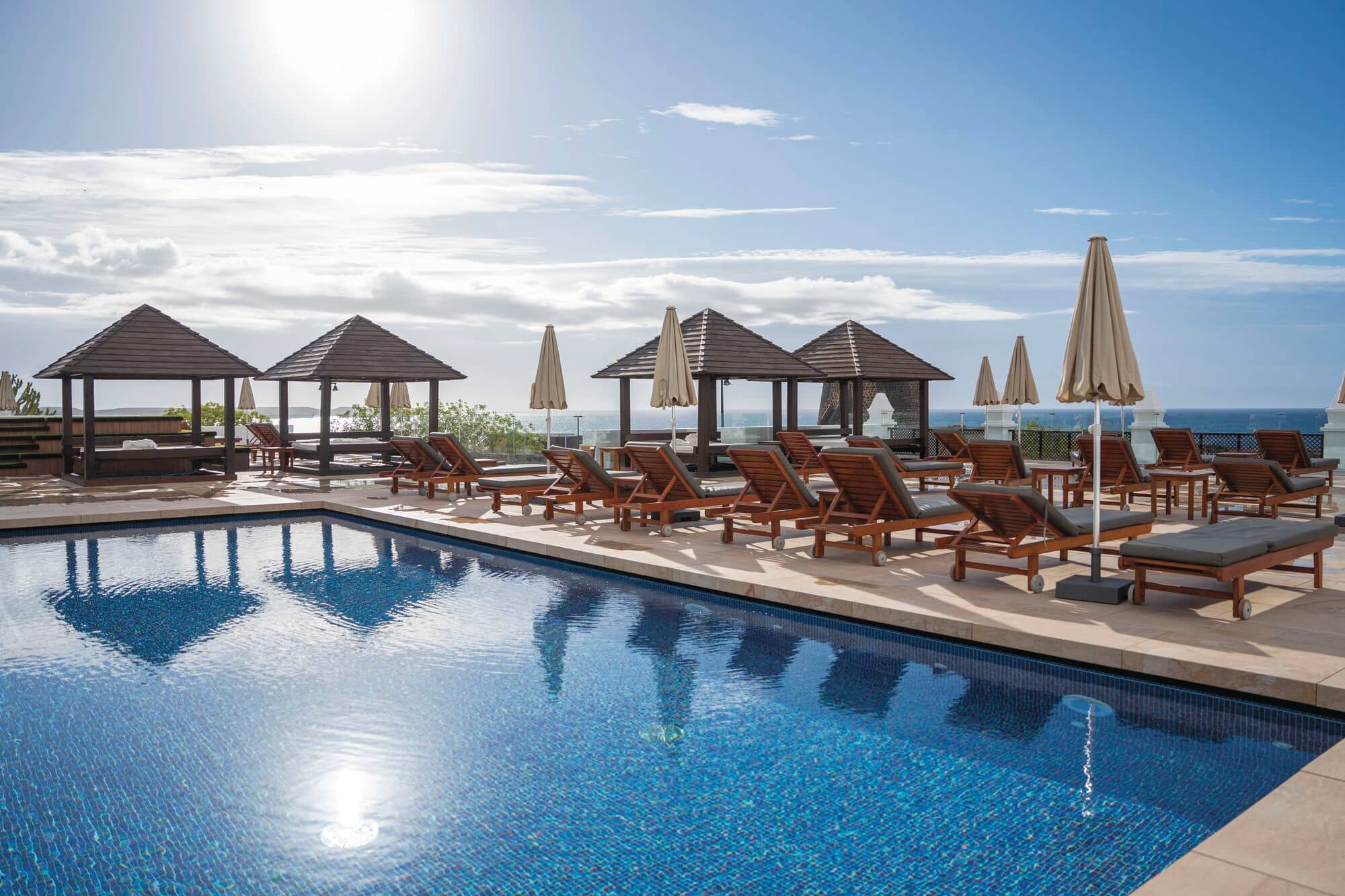 A blue swimming pull surrounded by sun loungers and parasols