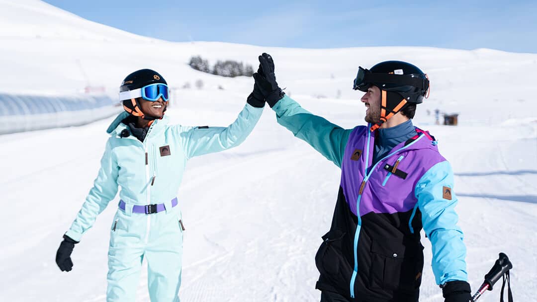 A man and a woman in ski gear high fiving on the slopes. 