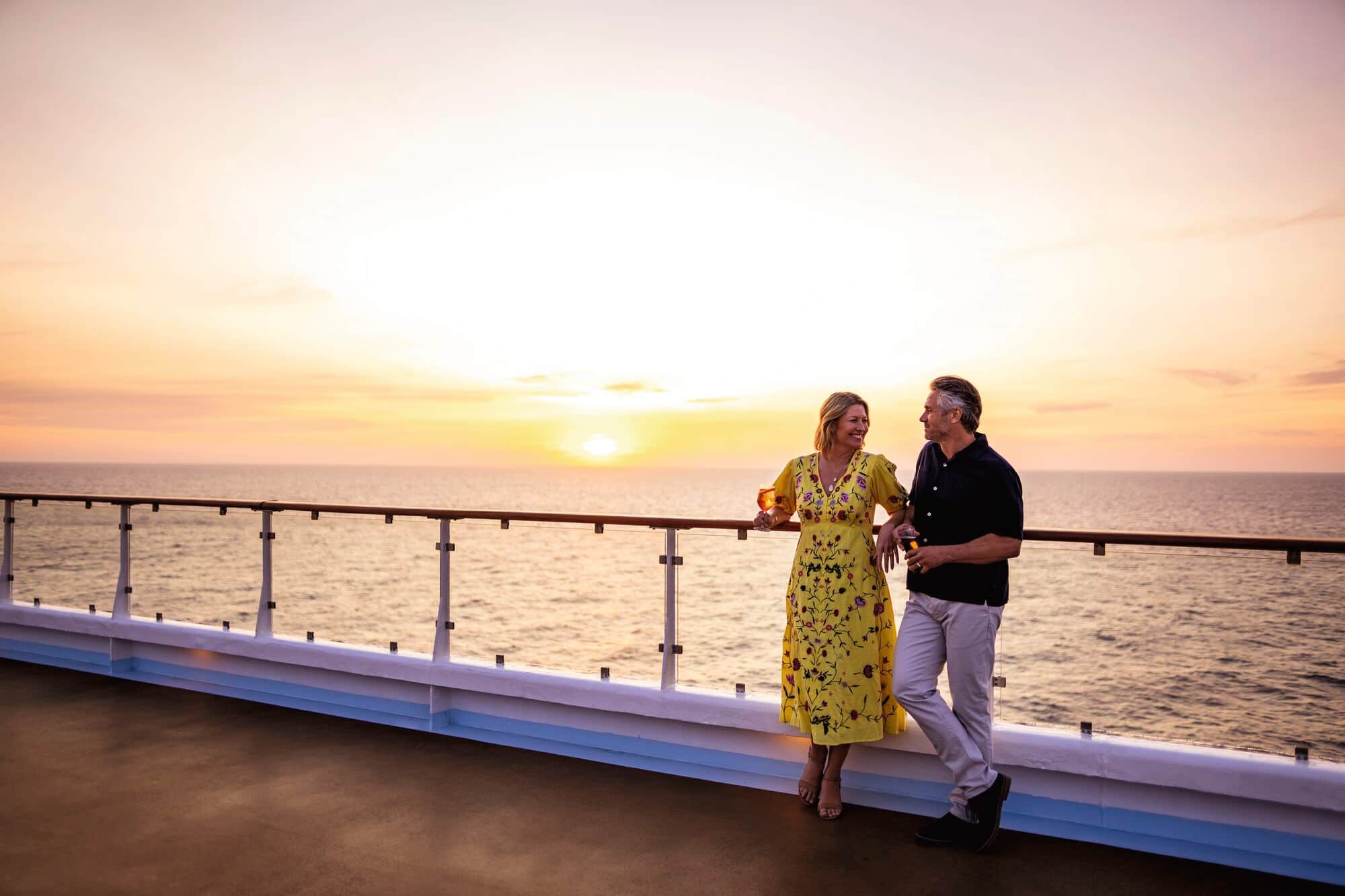 A couple smiling together on the top deck at sunset.
