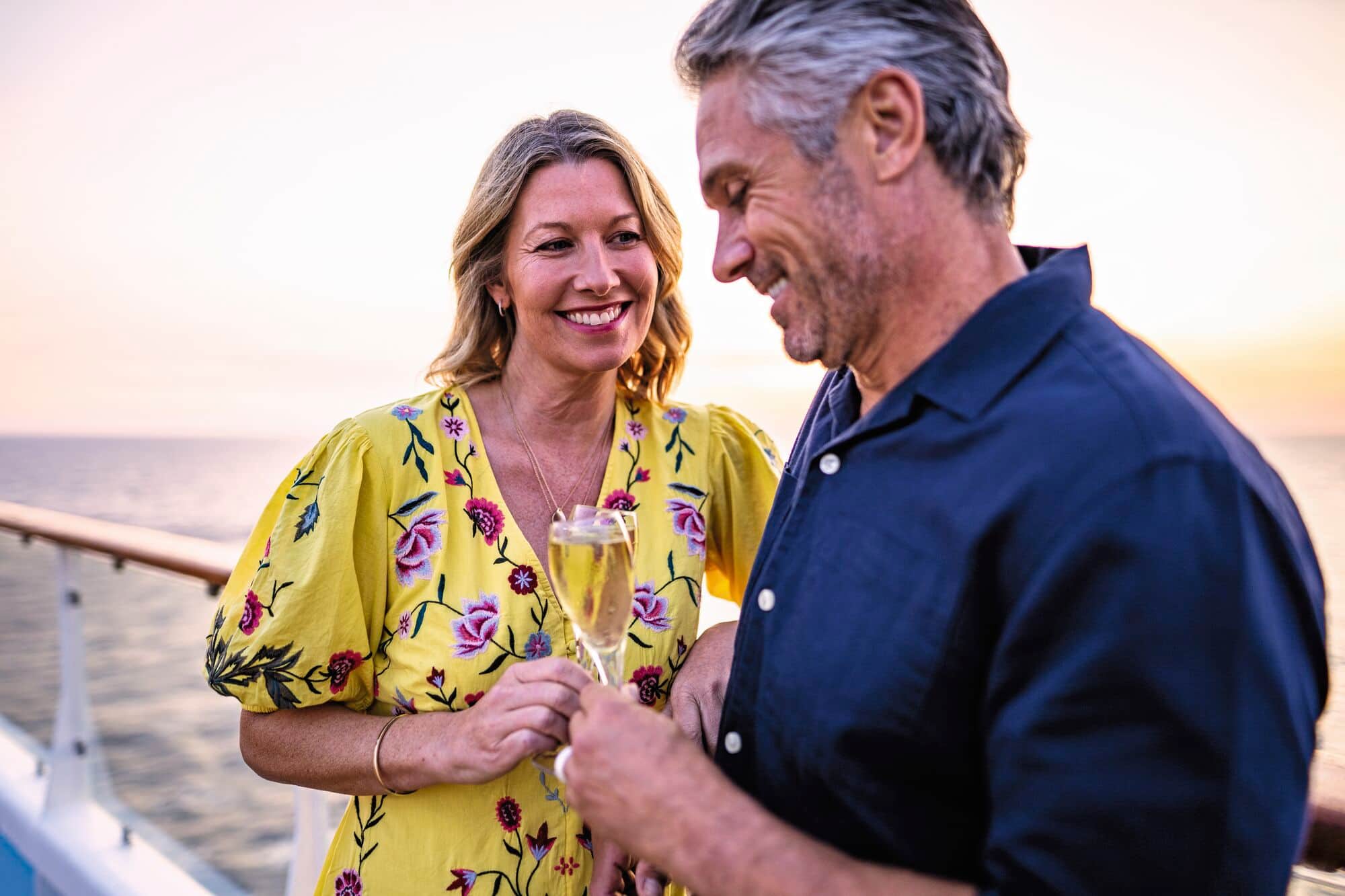 A happy couple toasting with champagne on a cruise ship deck at sunset.
