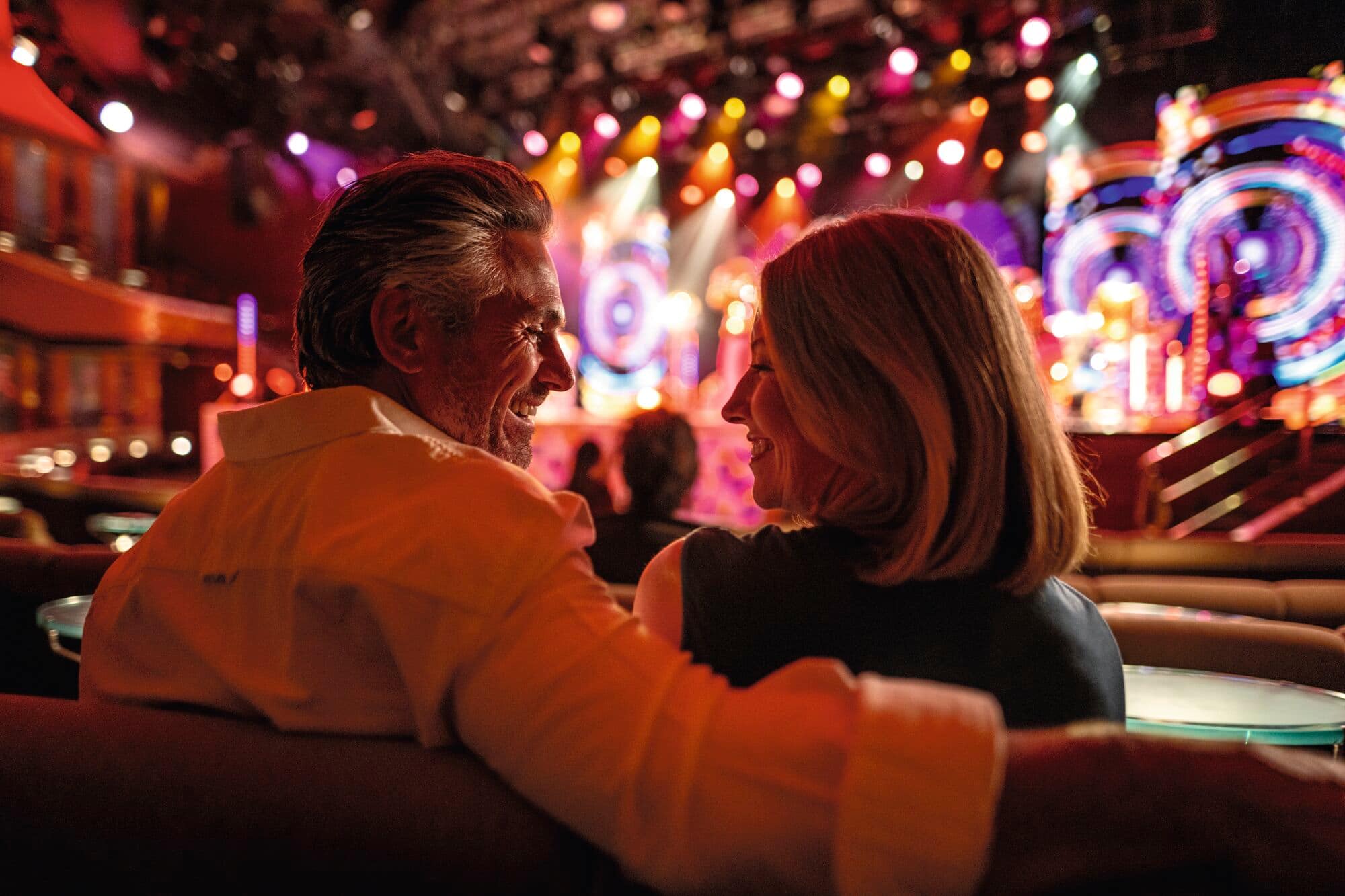 A smiling couple hug as a stage show's coloured lights shine in the background.