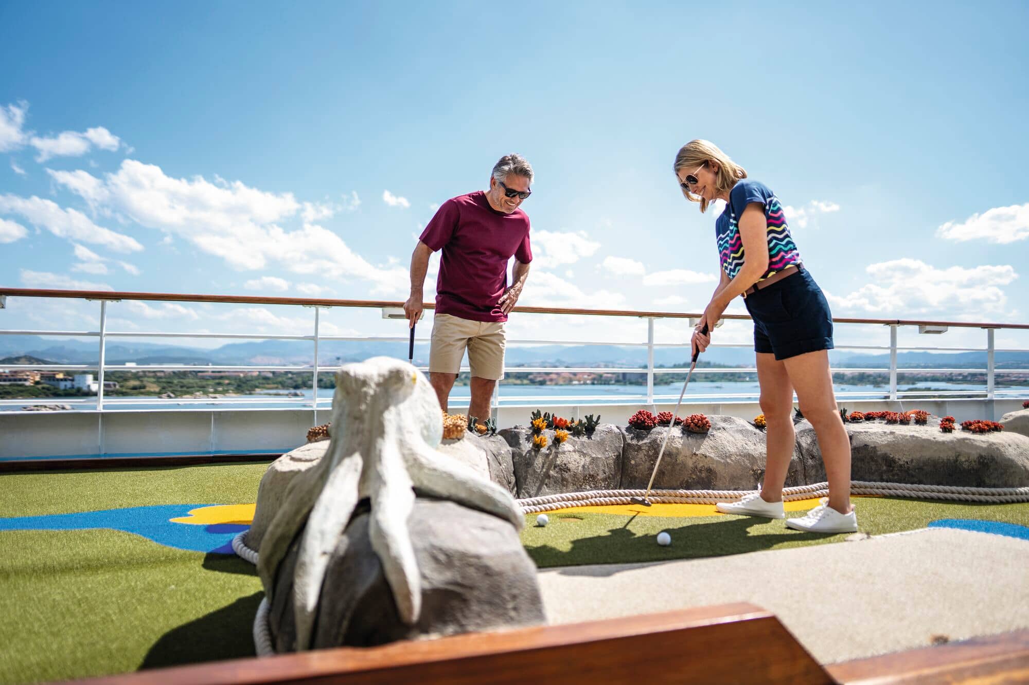A couple playing mini-golf on the top deck of a ship.